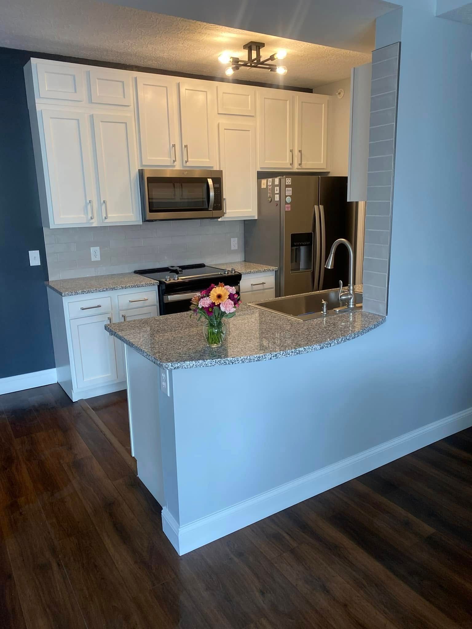 Open kitchen with white cabinets, granite peninsula, stainless appliances, and dark wood floors.