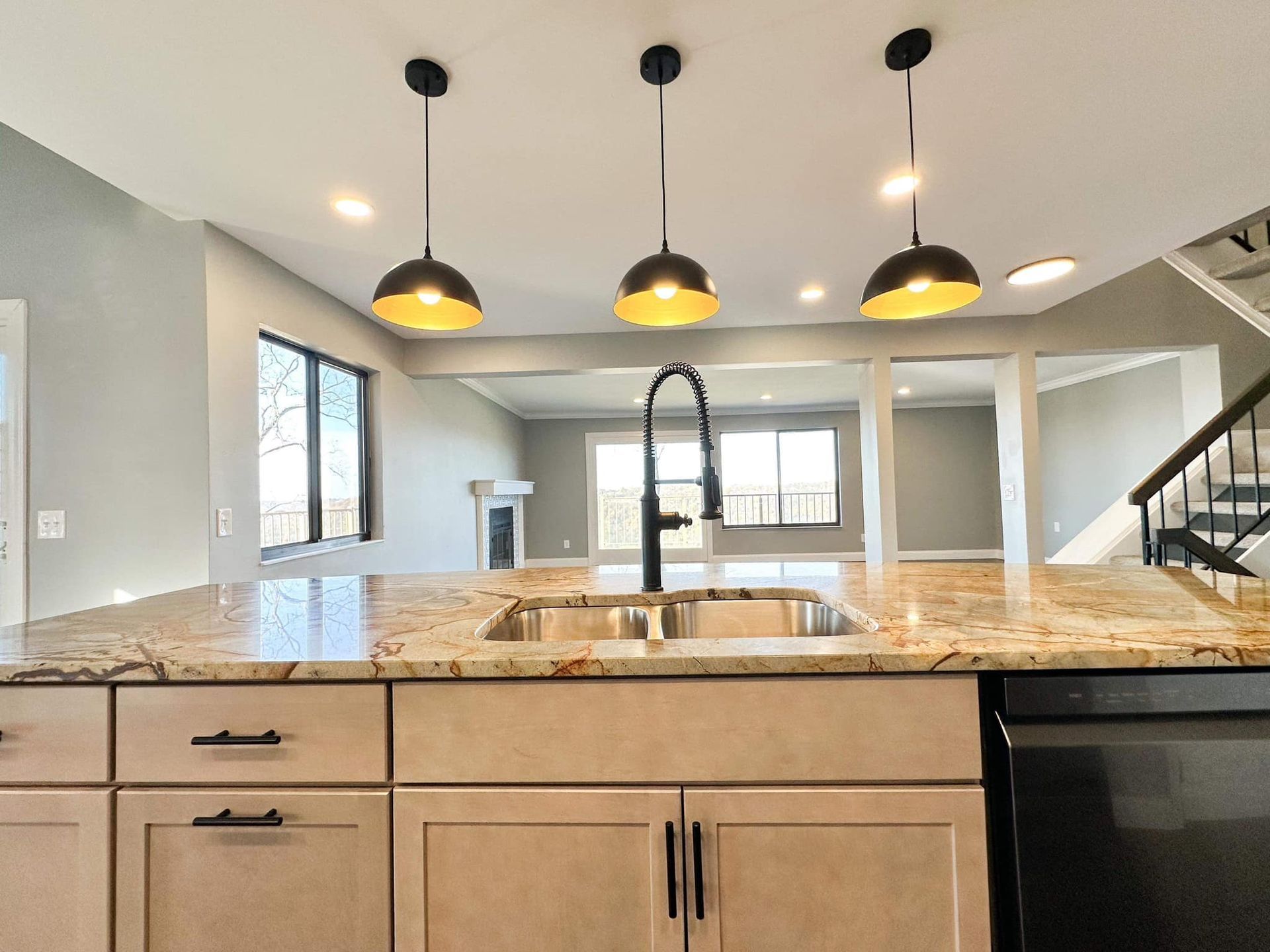 Modern kitchen with granite island, black pendant lights, and a staircase in the background