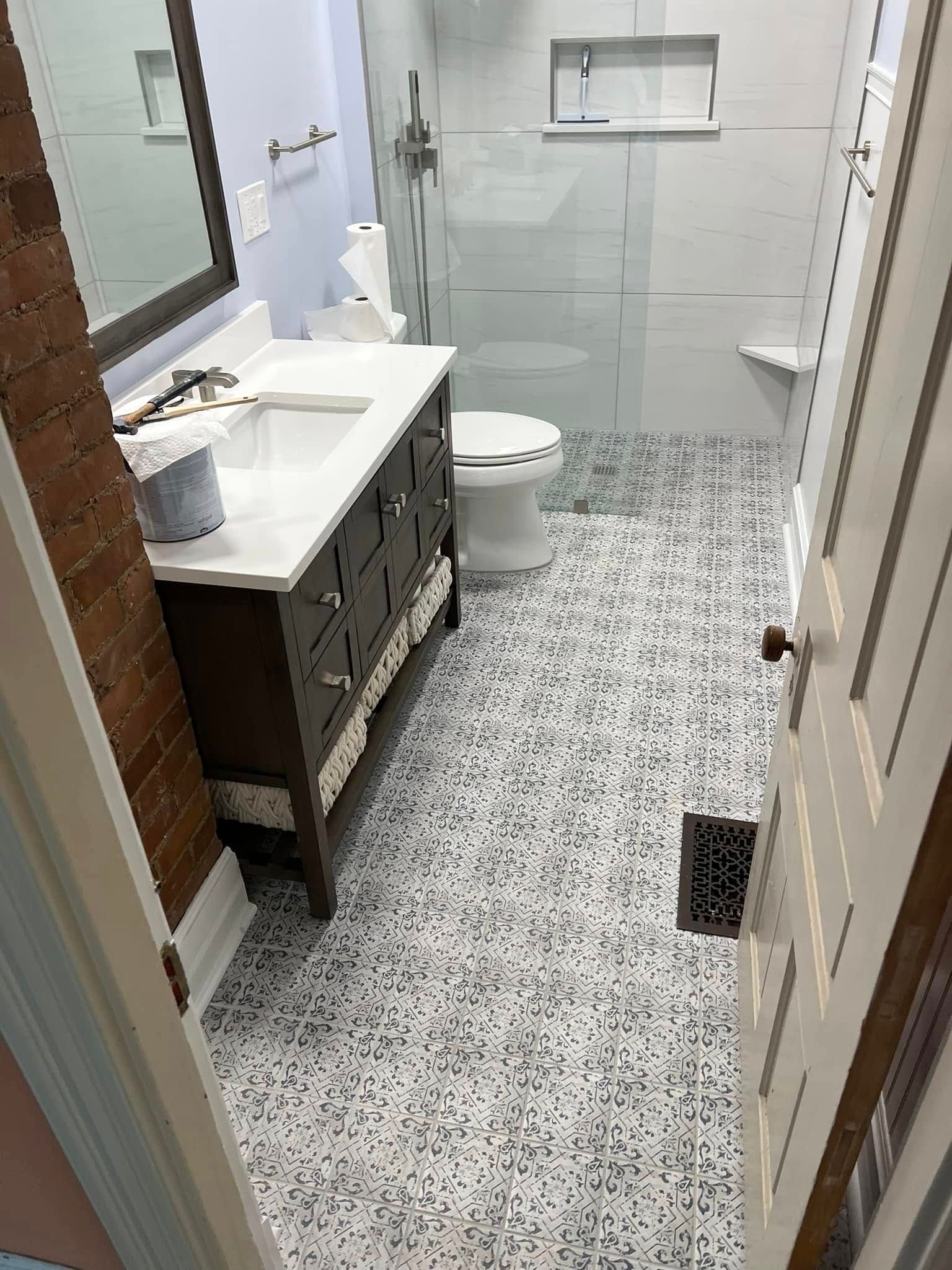 Narrow bathroom with white tile, speckled floor, vanity, toilet, shower, and open door.