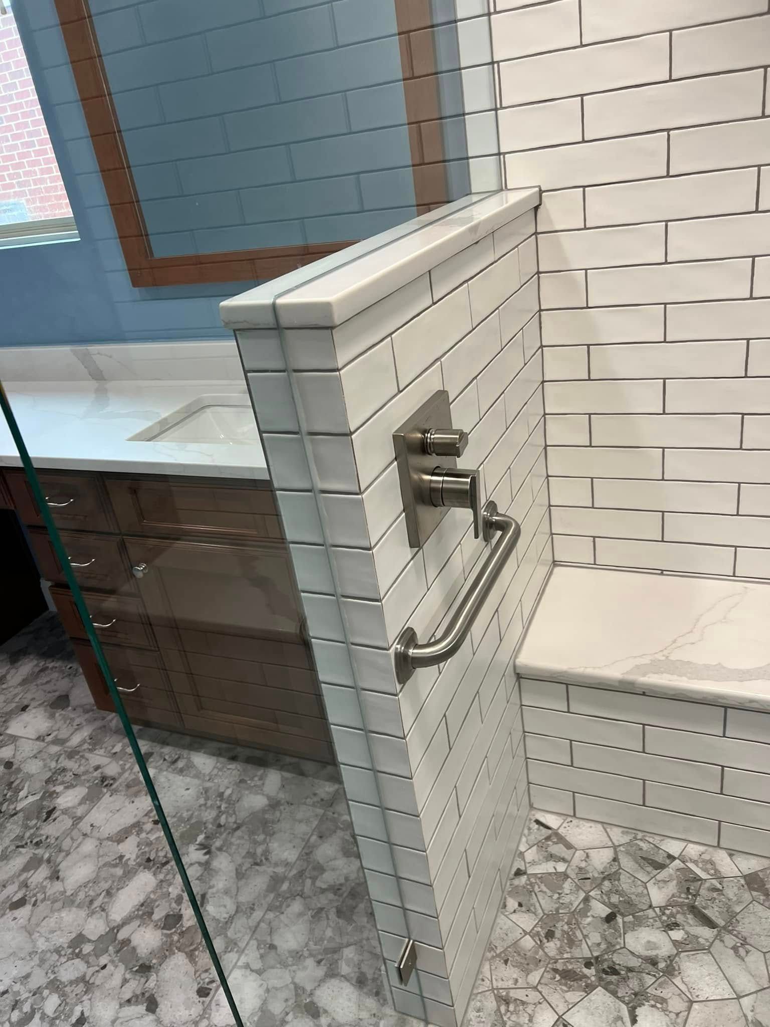Glass shower enclosure with white tiled walls, chrome handle, and gray floor tiles