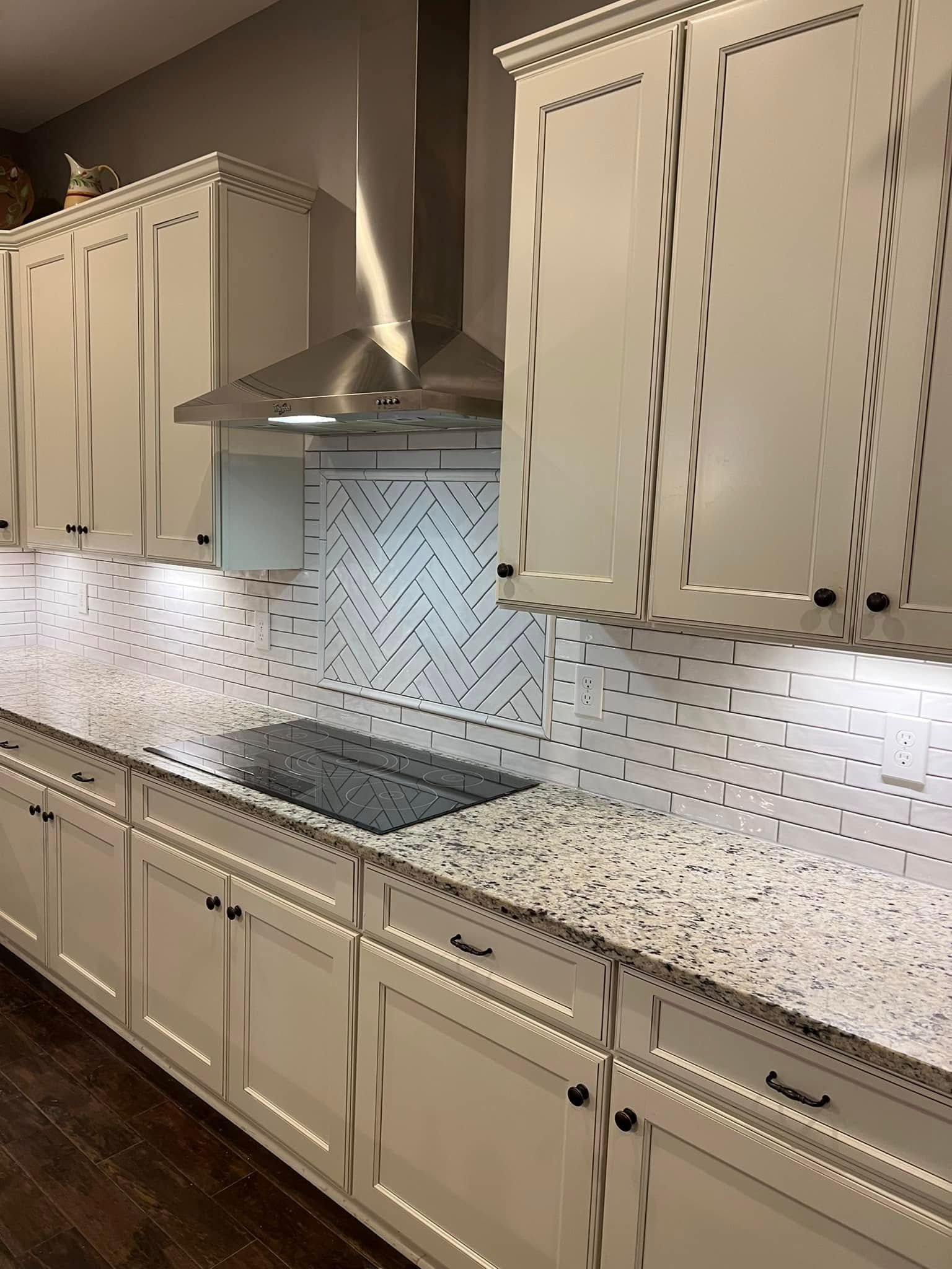 Modern kitchen with cream cabinets, speckled countertops, stainless range hood, and white tile backsplash