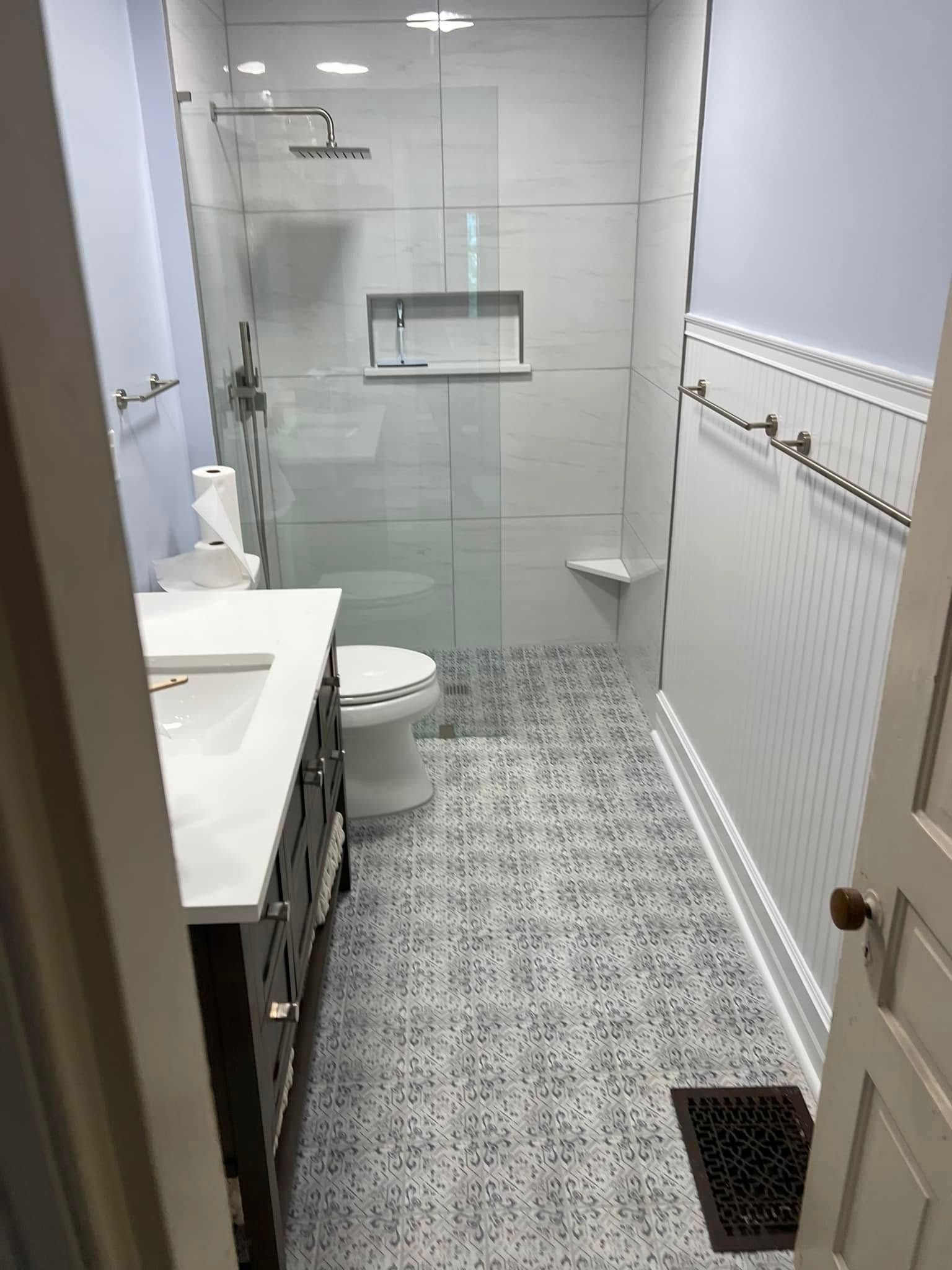 Narrow modern bathroom with glass shower, white sink, tiled floor, radiator, and wall-mounted towel rail.