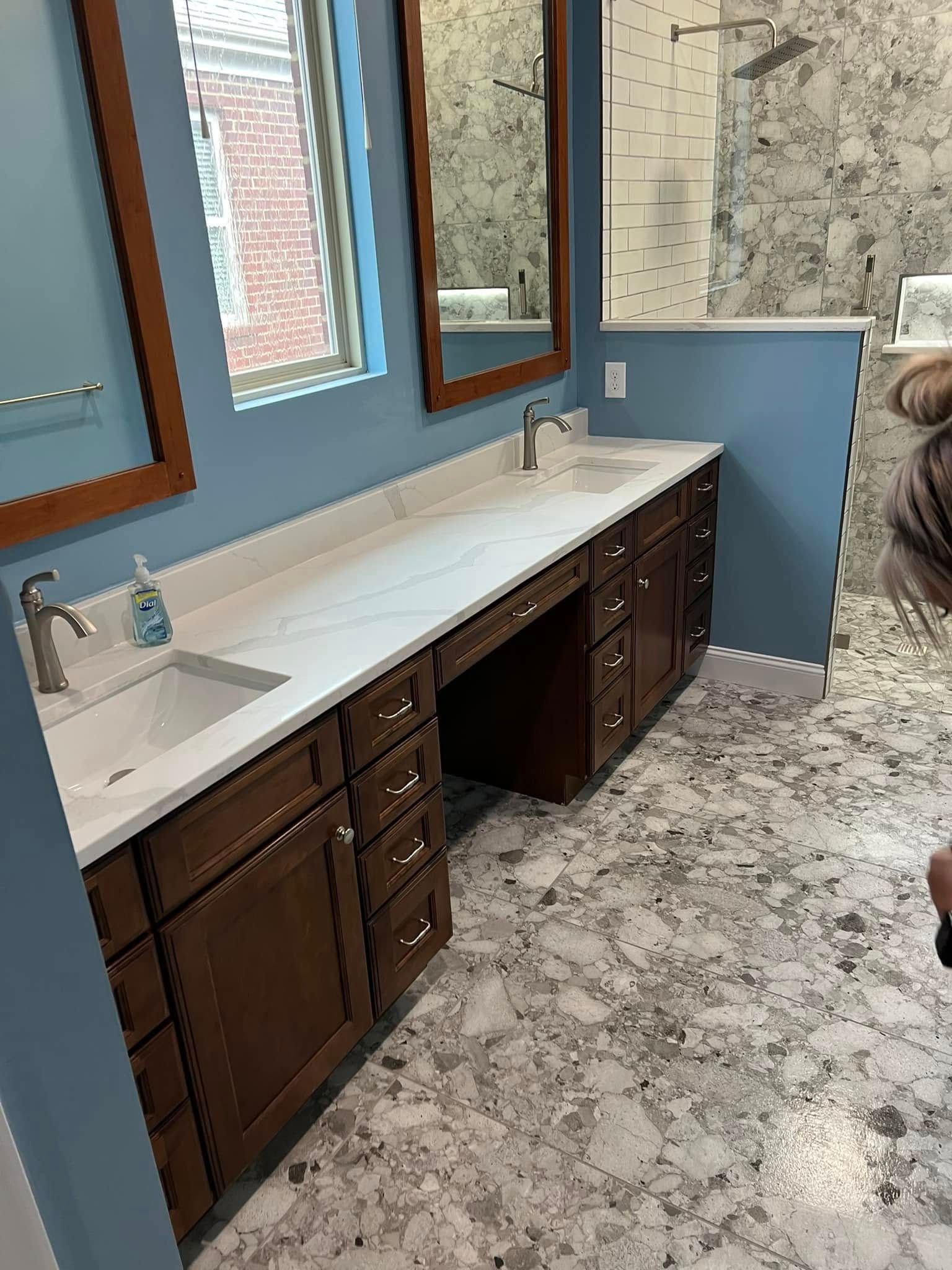 Bathroom vanity with double sinks, dark wood cabinets, and blue walls beside a tiled shower.