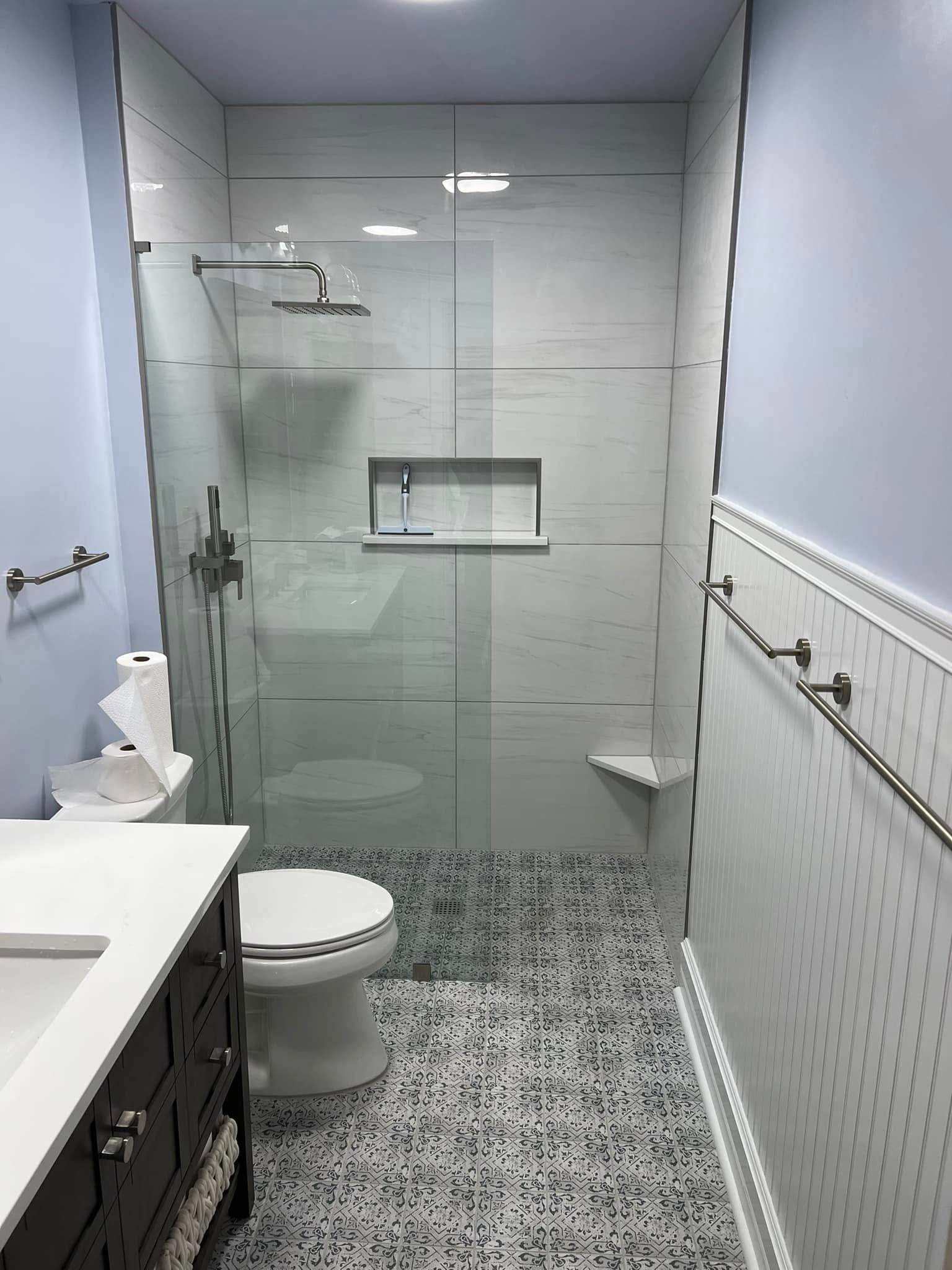 Narrow bathroom with tiled shower, toilet, vanity, and patterned floor tiles