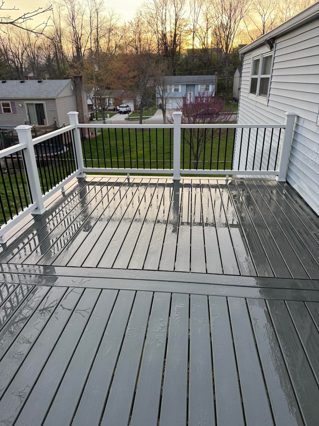 Wooden deck with white railings overlooking a green backyard at sunset