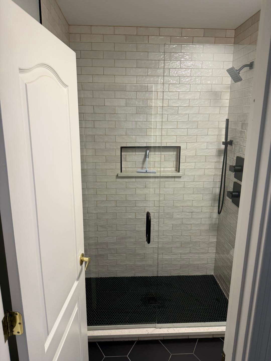 Small walk-in shower with white subway tile, black shower floor, and open white door.