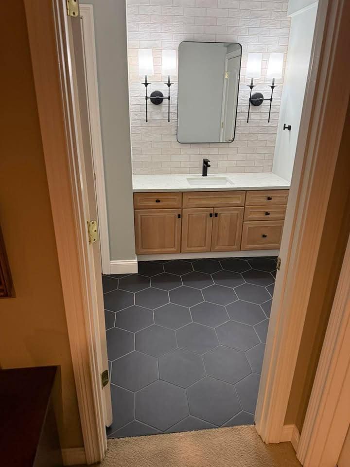 Bathroom vanity with wood cabinets, black hex tile floor, and a mirror above a sink.