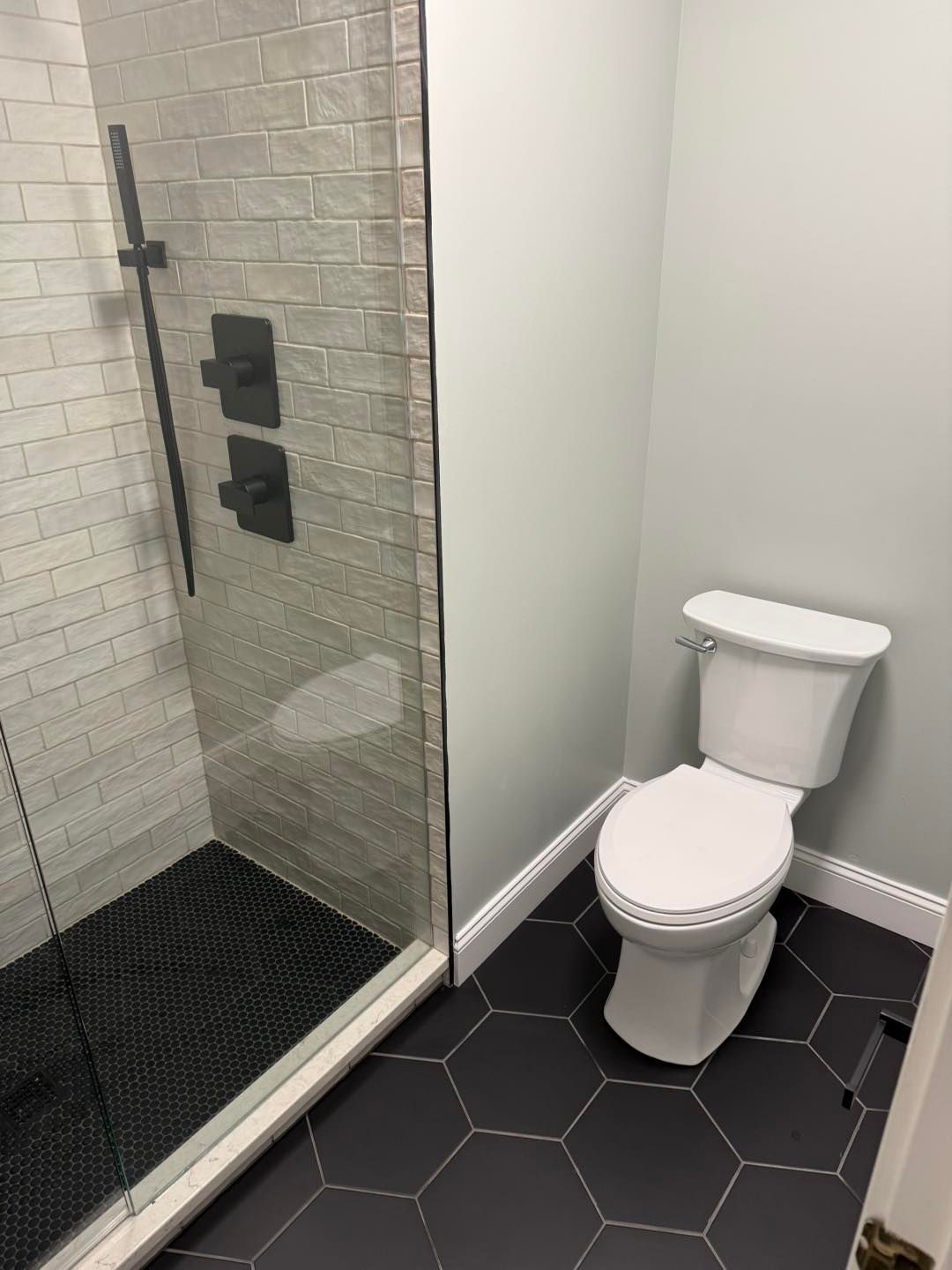 Small bathroom with glass shower, toilet, white walls, and black hexagon tile floor