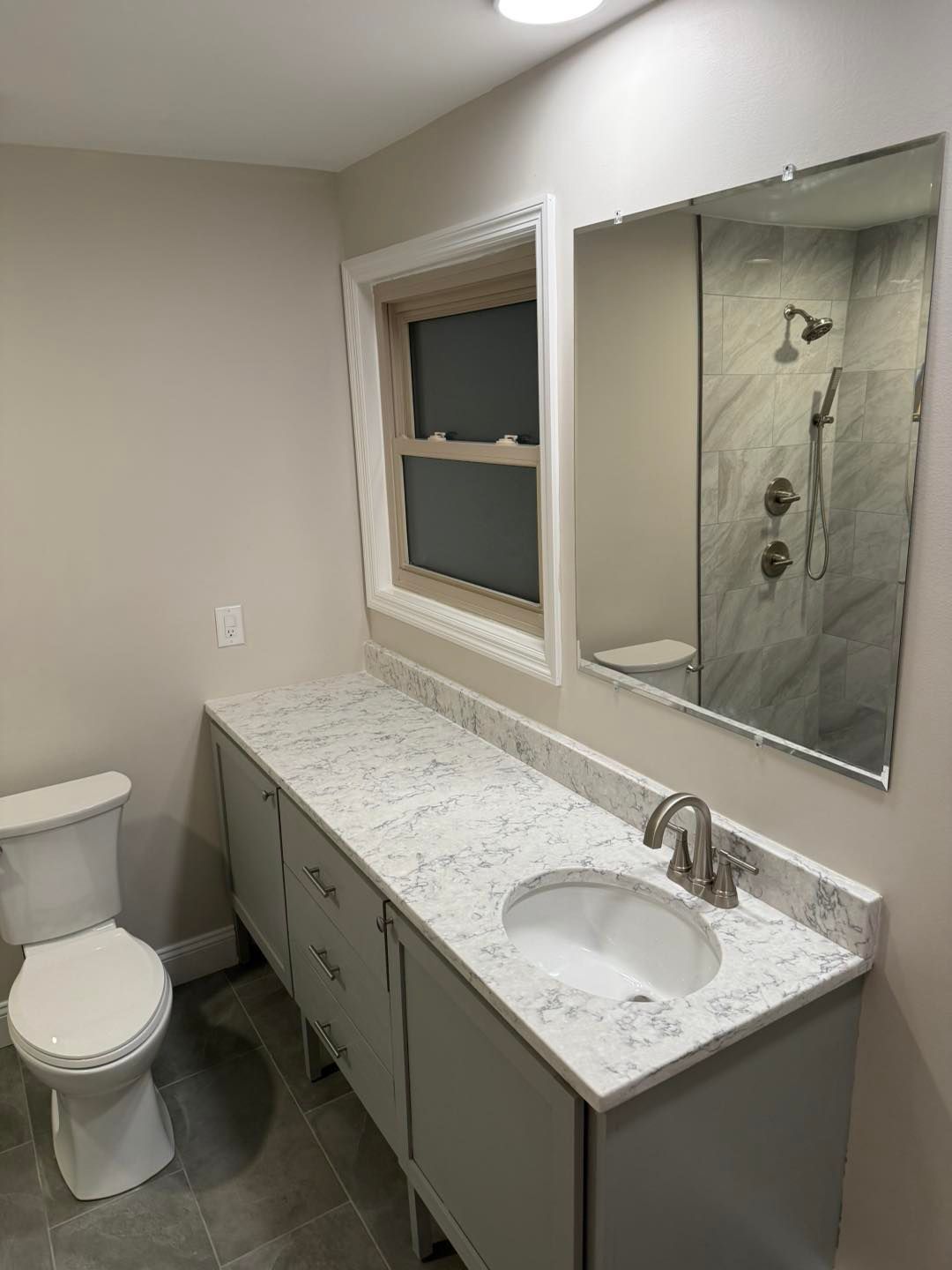 Small bathroom with toilet, long vanity, mirror, and tiled shower.
