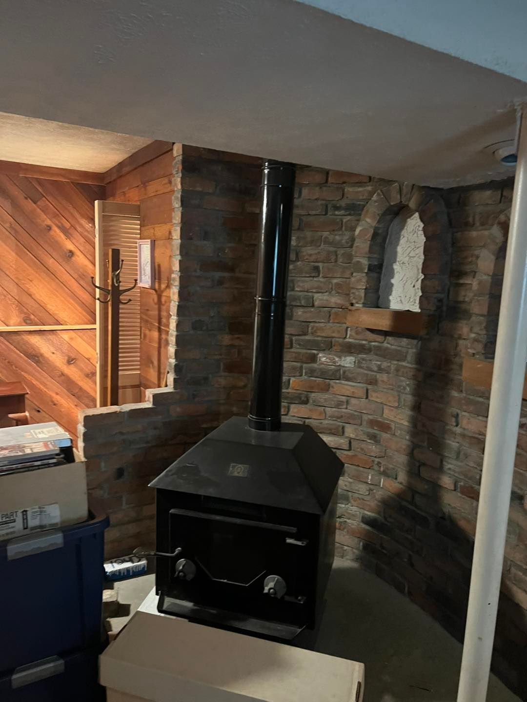 Brick fireplace with black wood stove and chimney in a cozy basement room