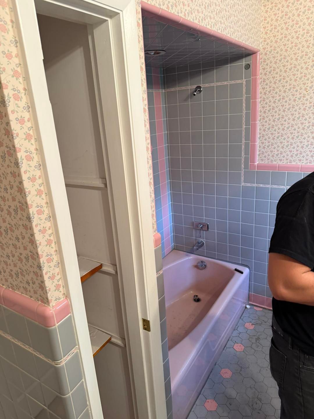 Bathroom with gray tile, pink accents, and a bathtub; part of a person standing at right.