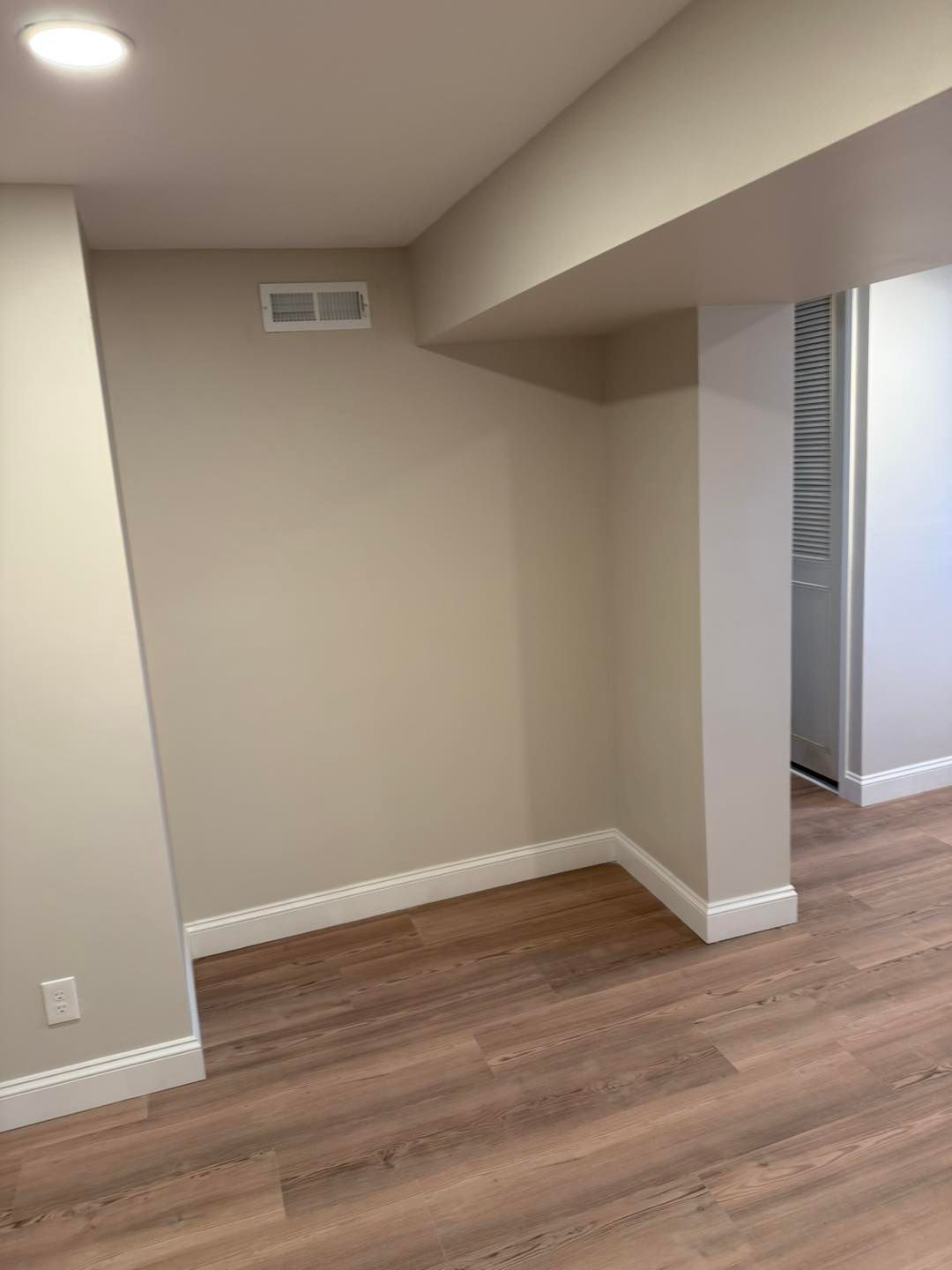 Empty beige room with wood flooring and a doorway opening to a hallway