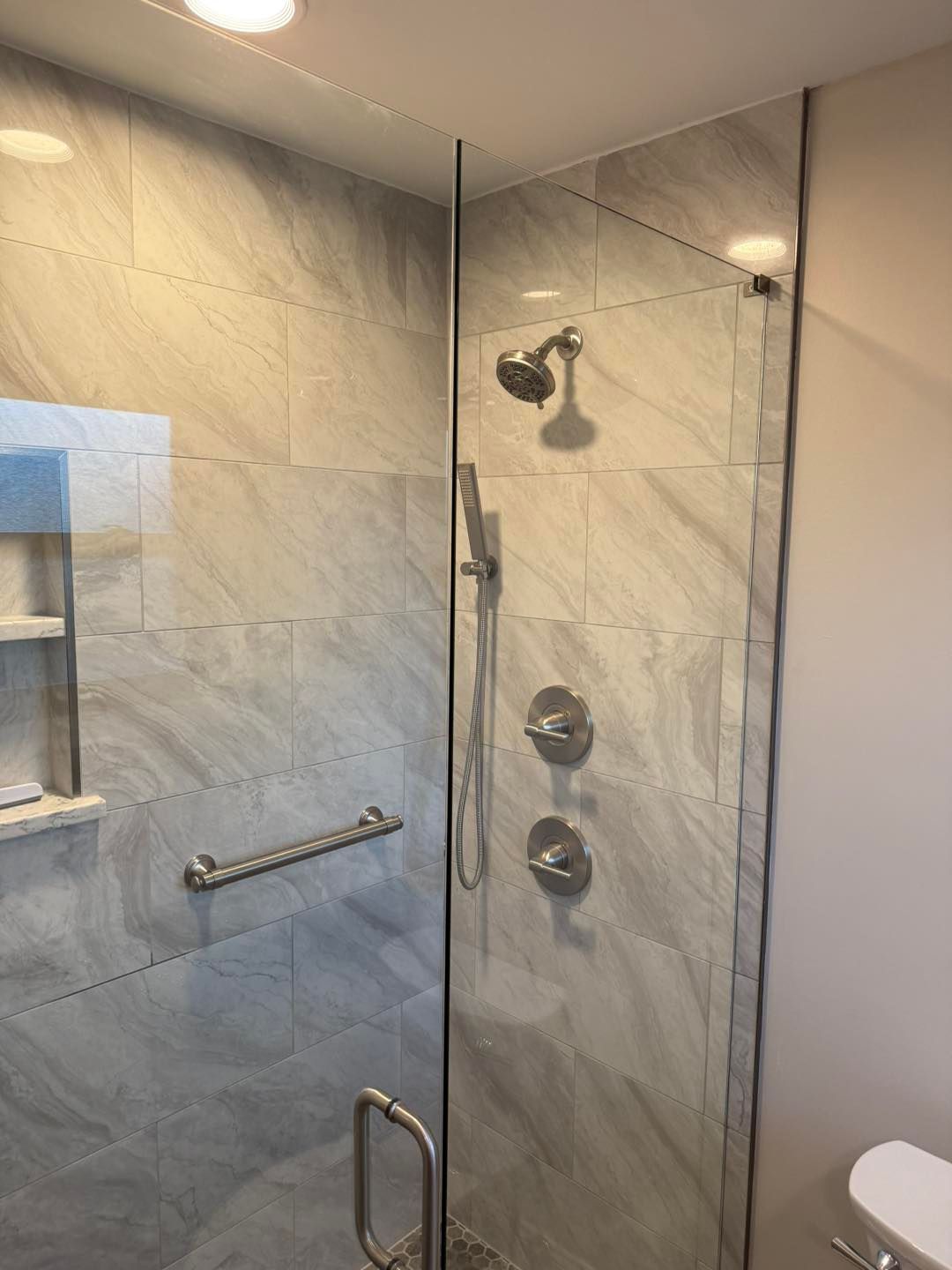 Glass shower with beige tile, chrome fixtures, and a grab bar.