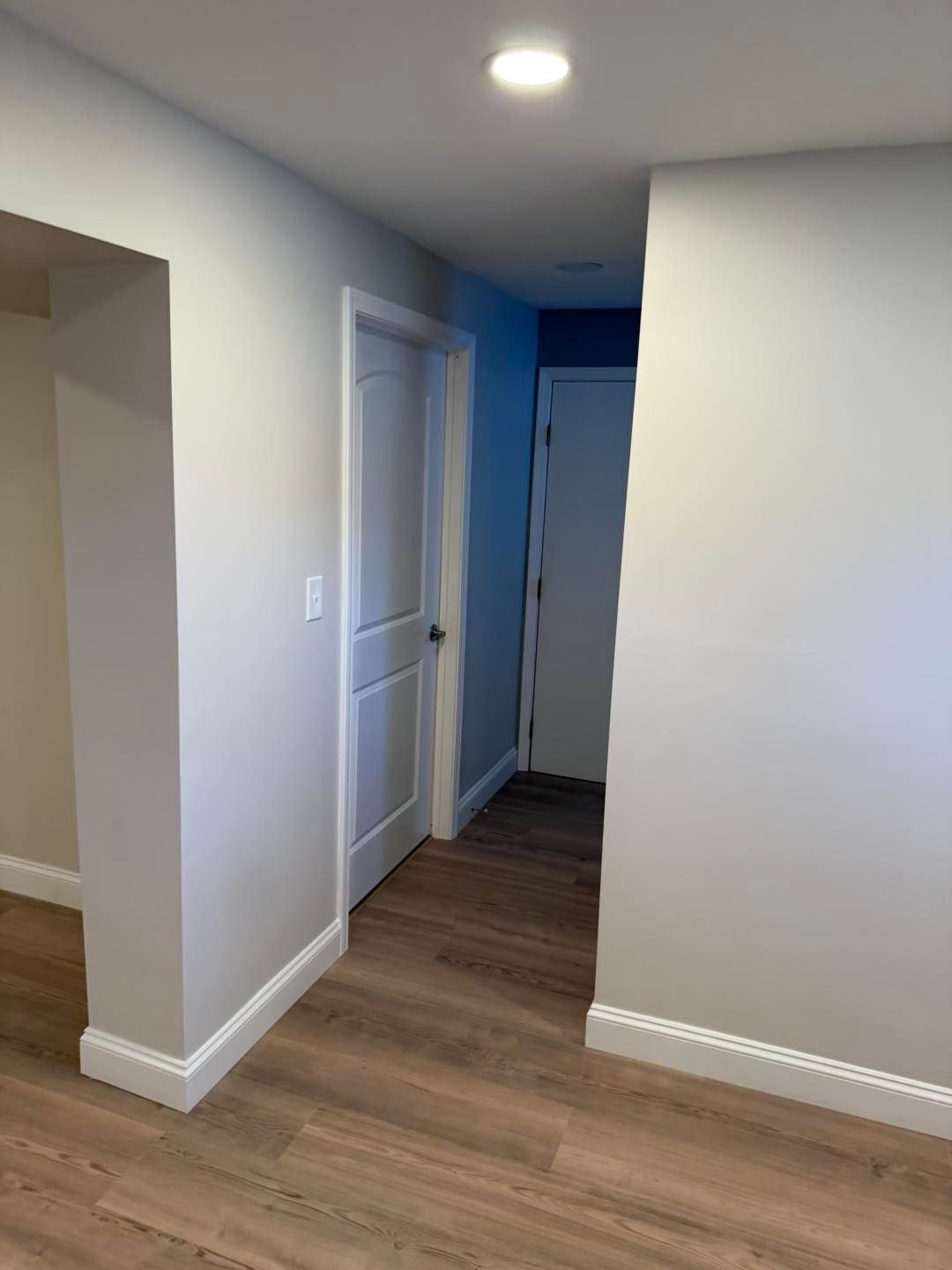 Empty hallway with light wood flooring, gray walls, recessed lights, and white trim and doors