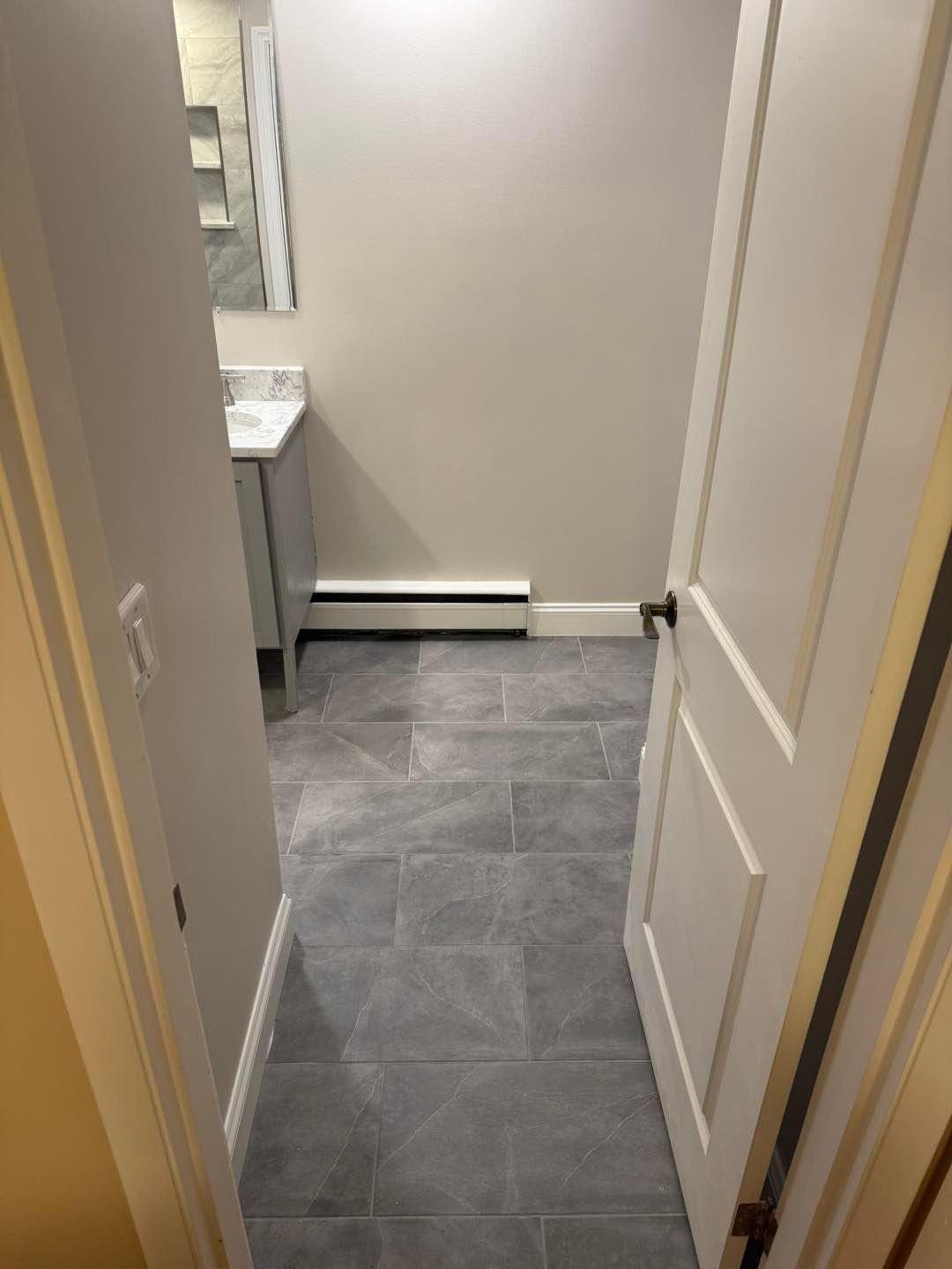 Narrow tiled hallway with a partially open white door and a small sink visible at the end.