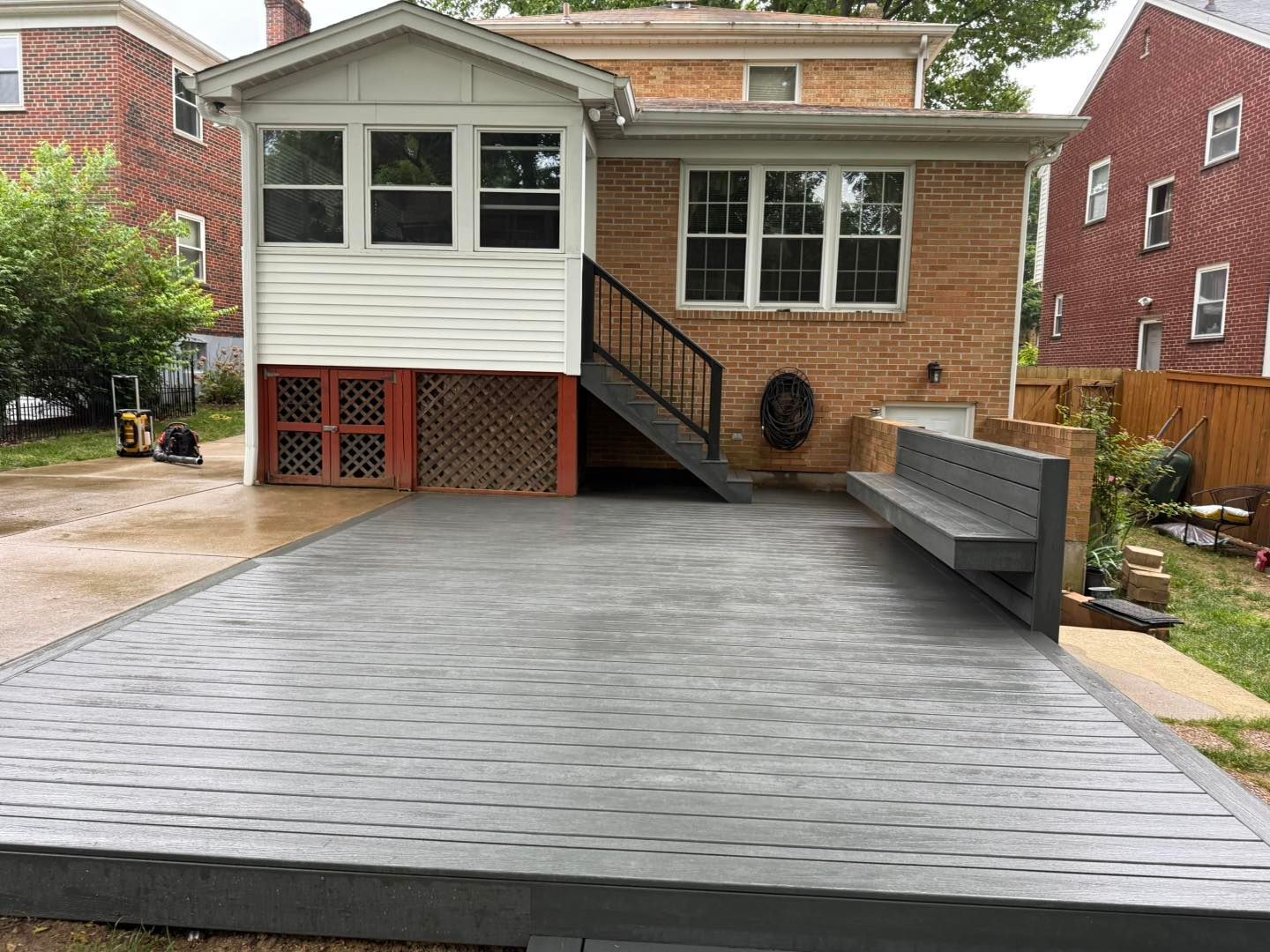 Driveway with a raised wooden deck and stairs leading to a brick house, viewed from the front.