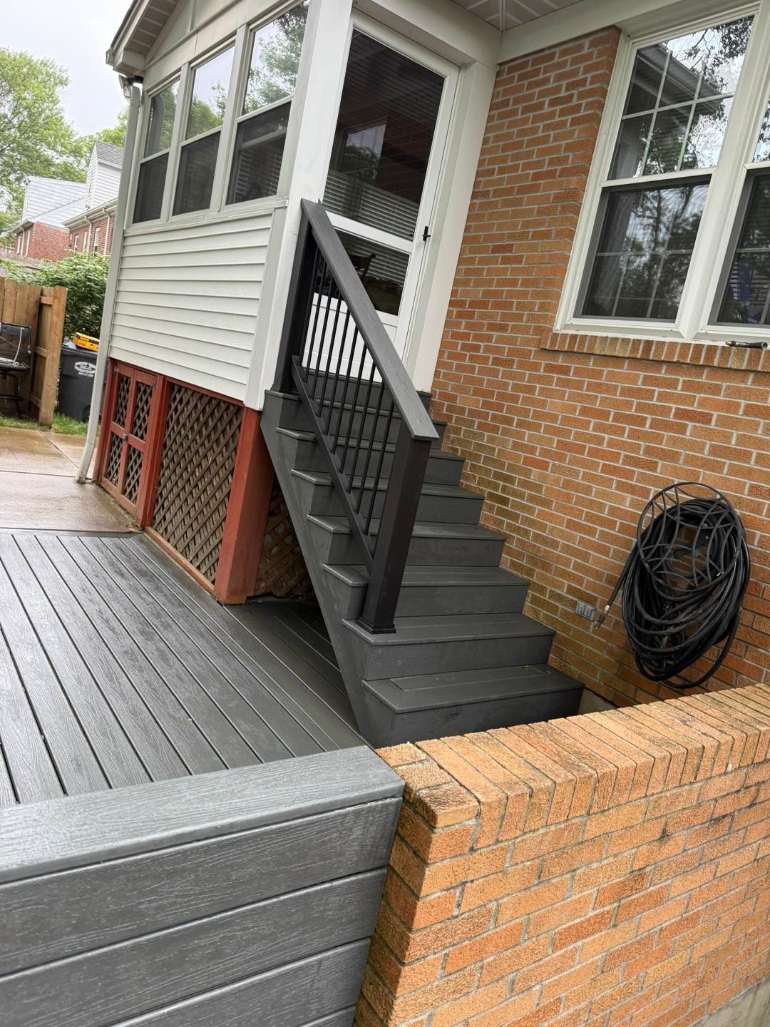 Backyard deck with black stairs leading to a screened porch beside a brick house