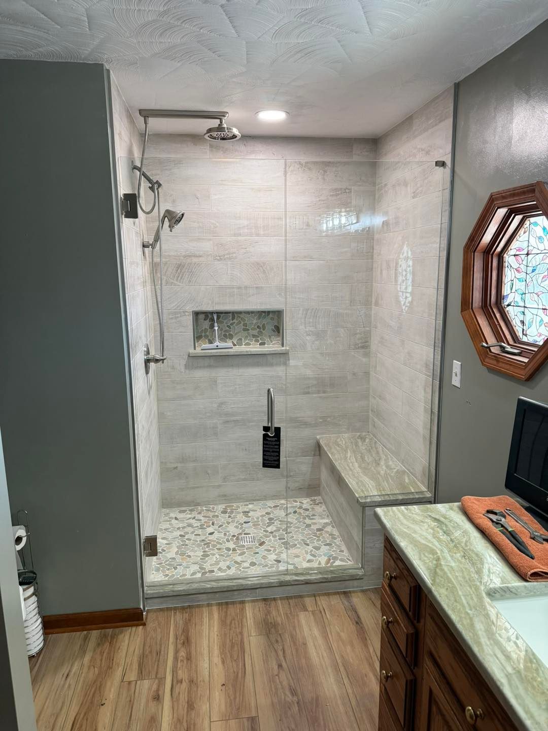 Modern bathroom with tiled shower, glassless opening, and wood-look floor beside a vanity window.