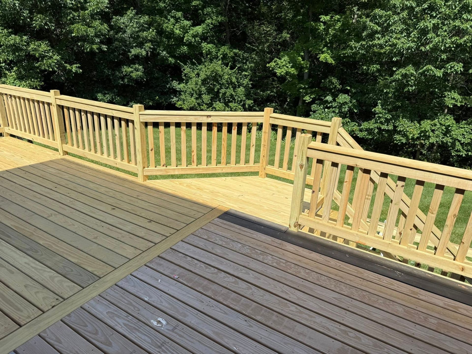 Wooden deck with tan railing overlooking a green wooded area