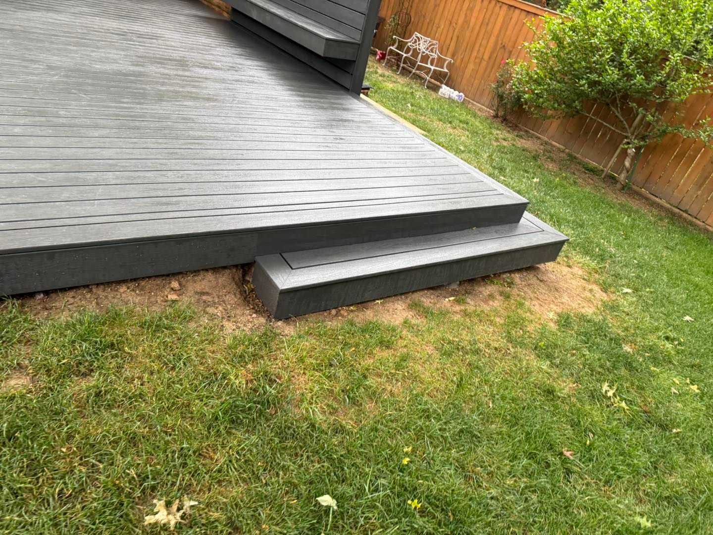 Gray backyard deck with a low step down to a grassy lawn and wooden fence.