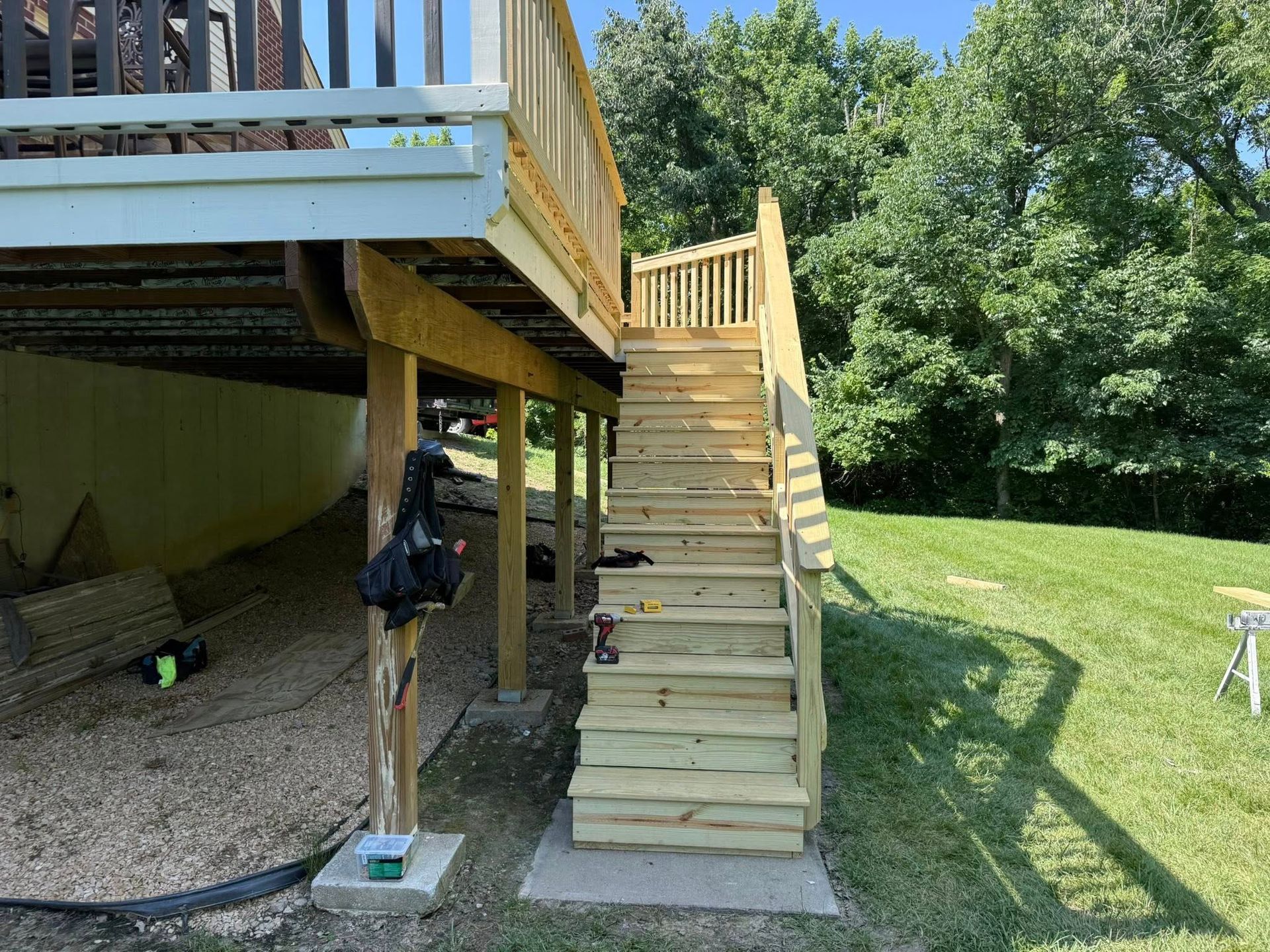 Wooden deck stairs leading to a raised backyard deck beside a grassy yard and trees