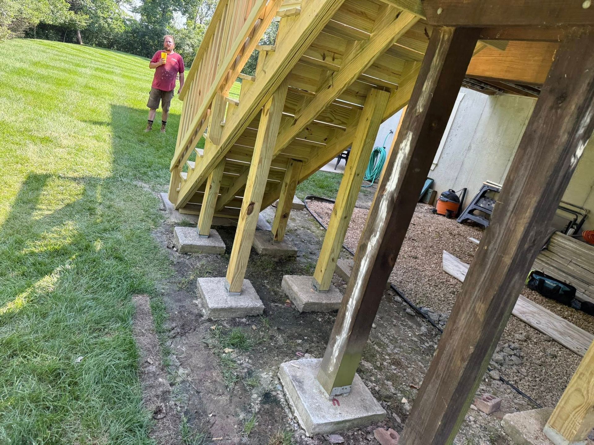 Wooden stairs on concrete footings beside a grassy yard, with a person standing in the background.