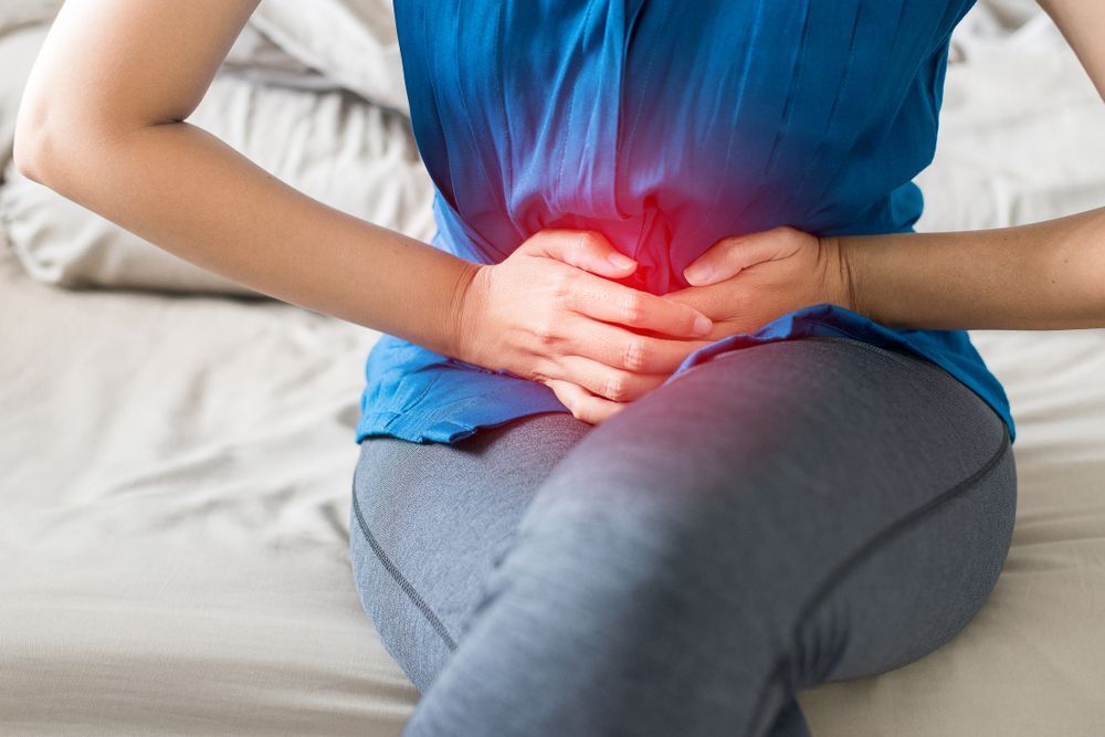 A Woman Is Sitting On A Bed Holding Her Stomach In Pain — Brisbane Upper GI Surgery in Chermside, QLD