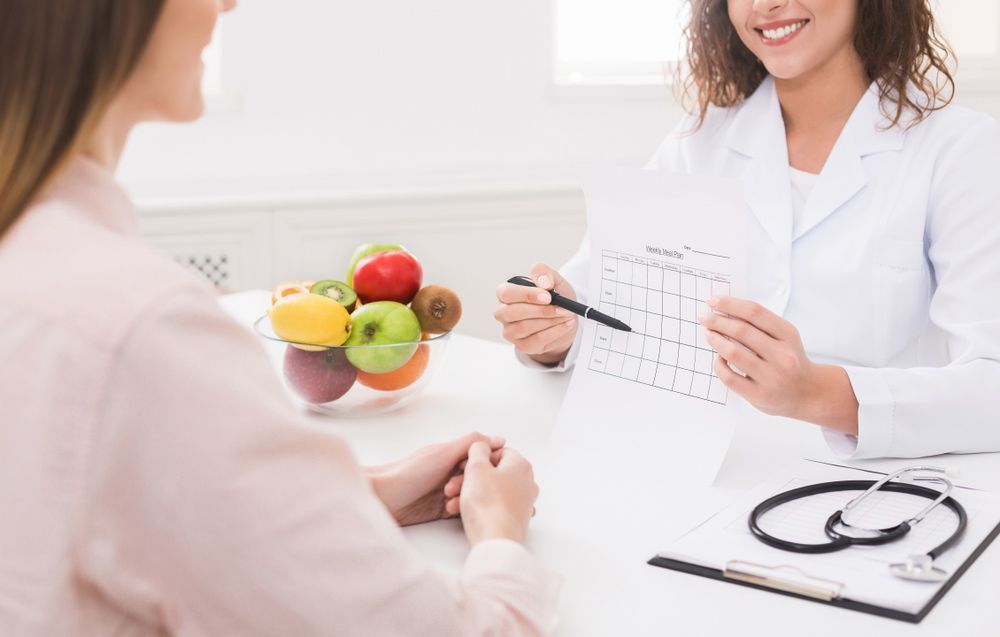 A Woman is Sitting at a Table Talking to a Doctor Who is Holding a Calendar — Brisbane Upper GI Surgery in Chermside, QLD