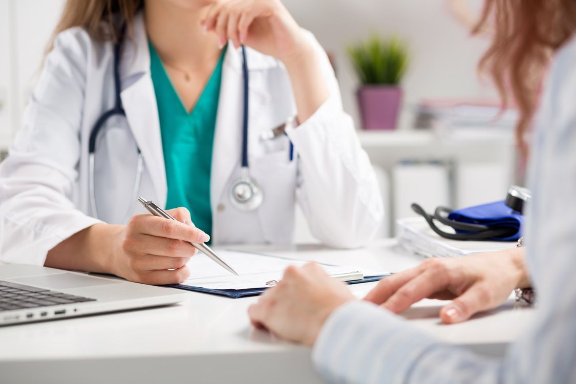 Doctor In White Coat Consulting With A Patient At A Desk, Writing On A Clipboard — Brisbane Upper GI Surgery in Chermside, QLD