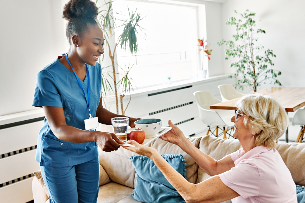 Caregiver serving drinks to seated residents in a bright, modern care home lounge