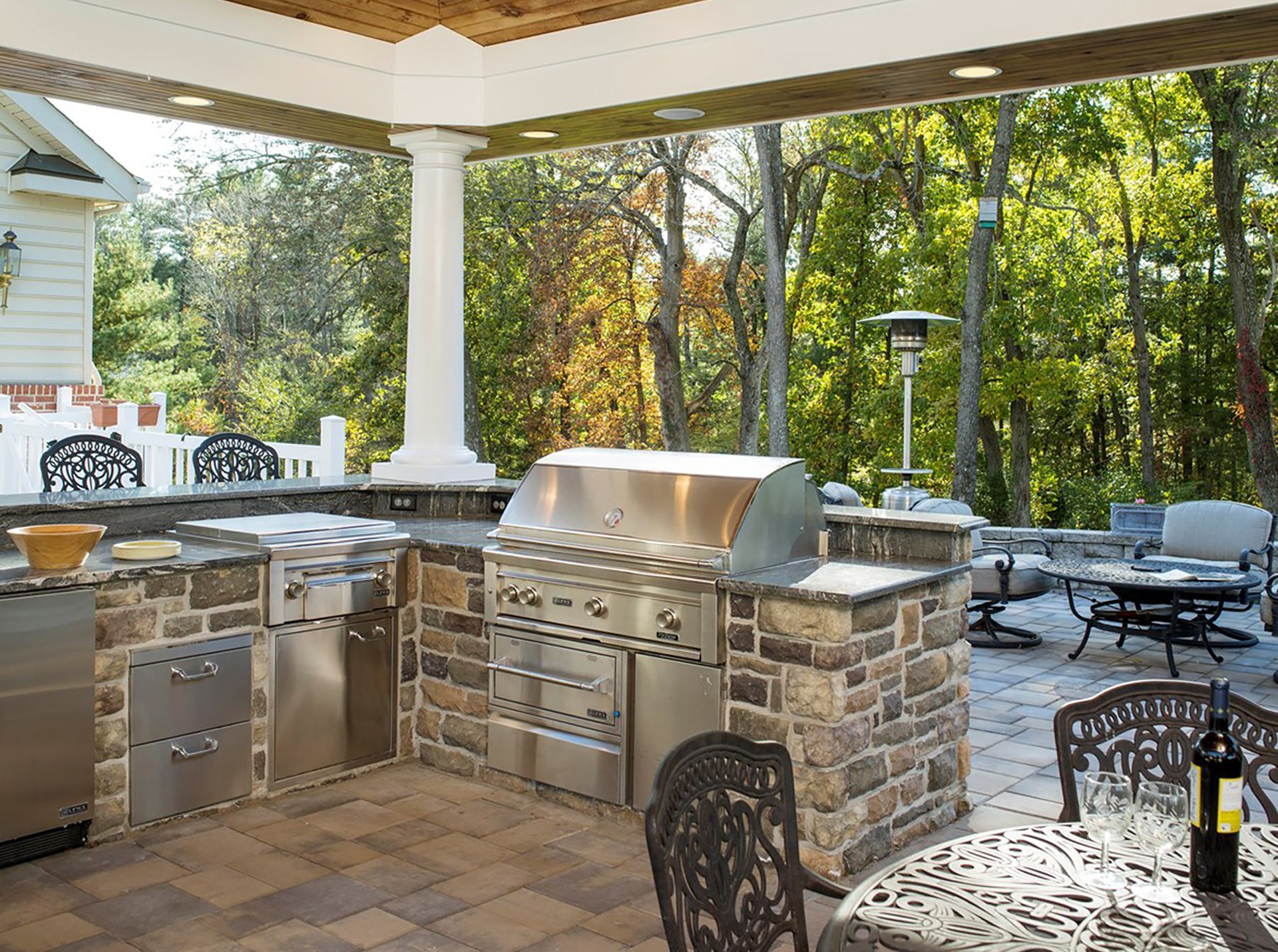 An outdoor kitchen with a stainless steel grill and a table and chairs