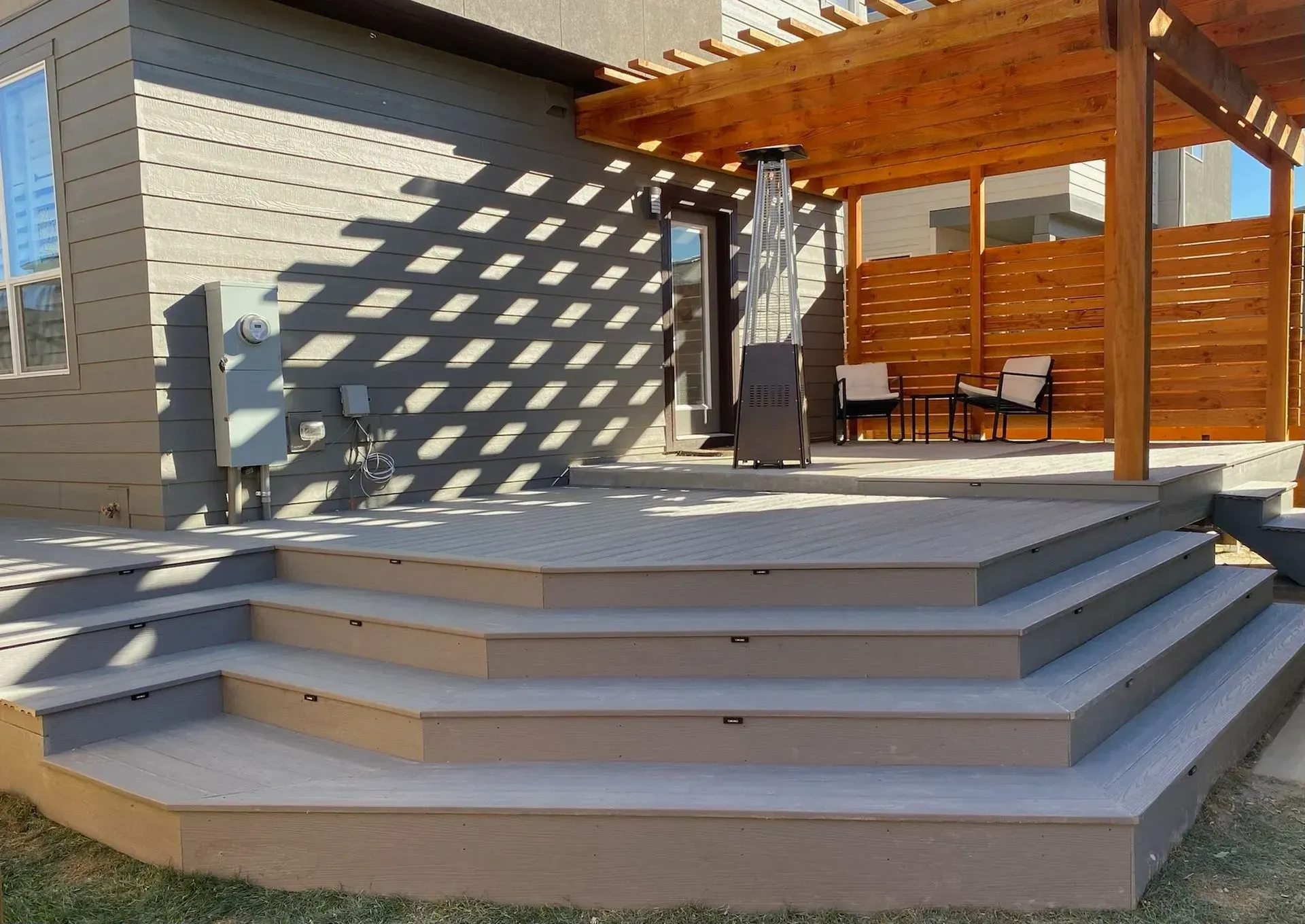 Outdoor deck with steps, pergola, and seating area. Brown wood and gray composite.