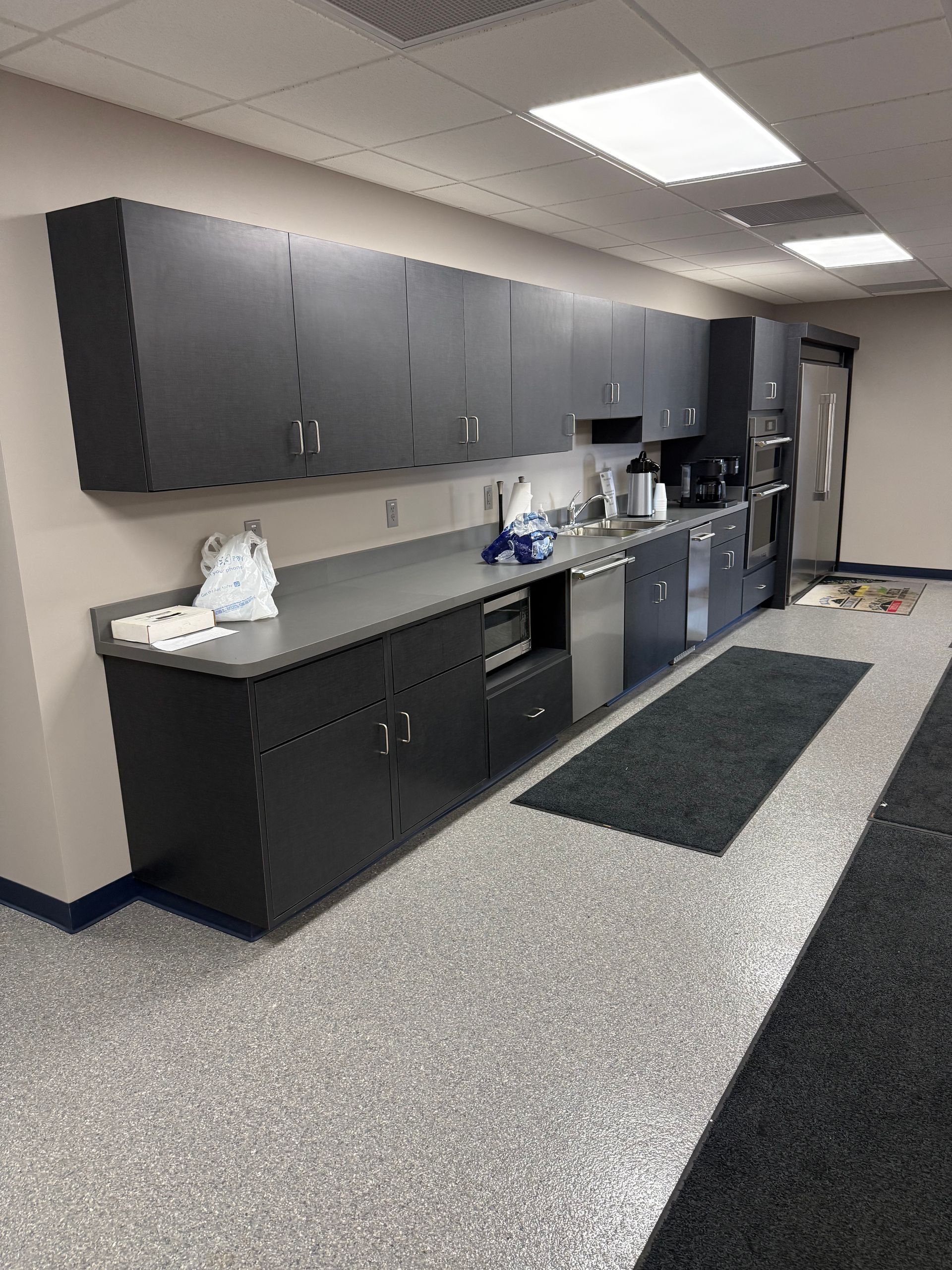 Break room with black cabinets, countertop, sink, coffee station, and gray speckled floor tiles