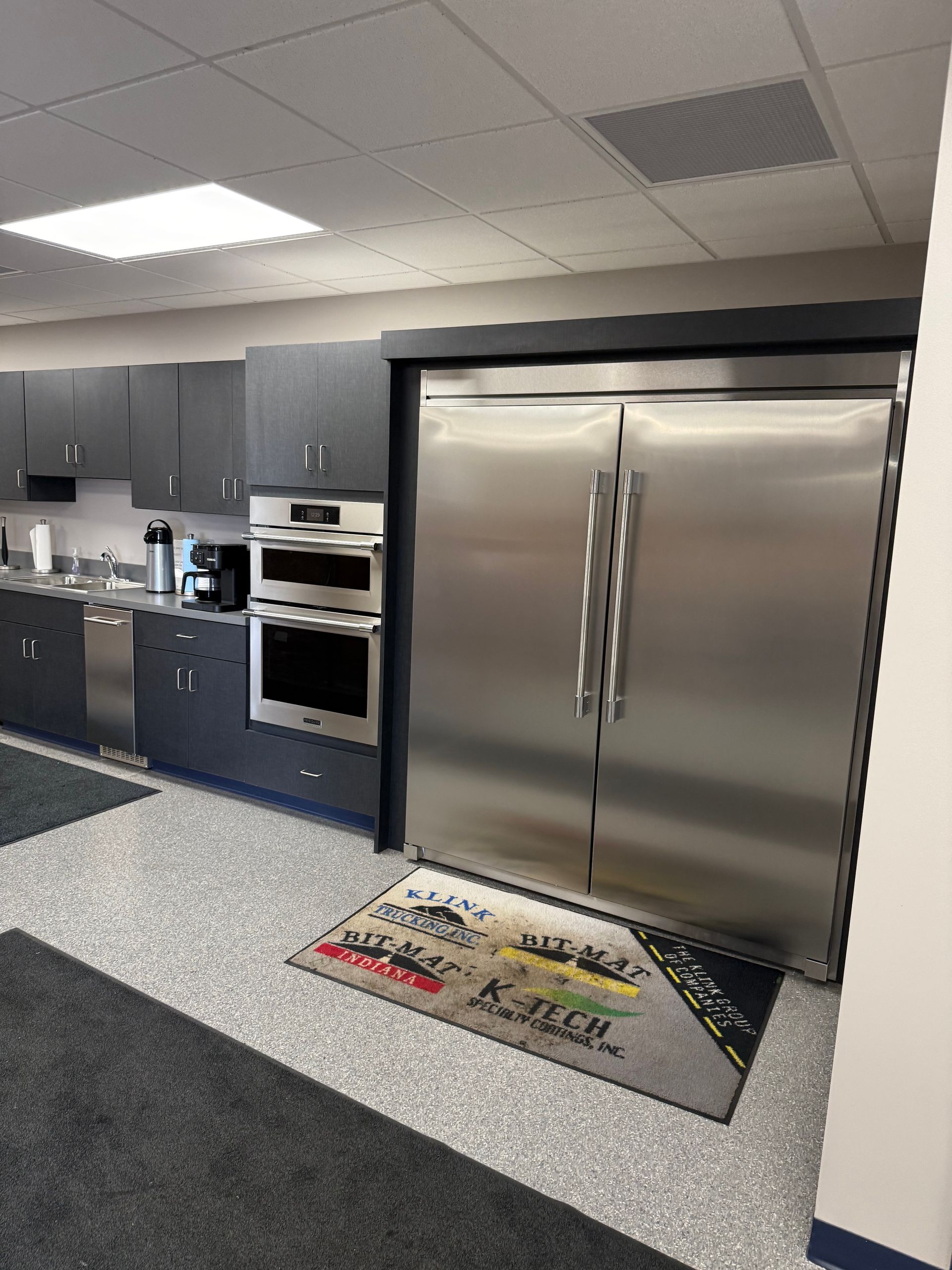 Commercial kitchen with stainless steel double doors, gray cabinets, and a speckled floor mat