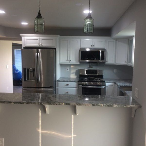 Modern kitchen with stainless steel appliances, granite breakfast bar, and two green pendant lights.