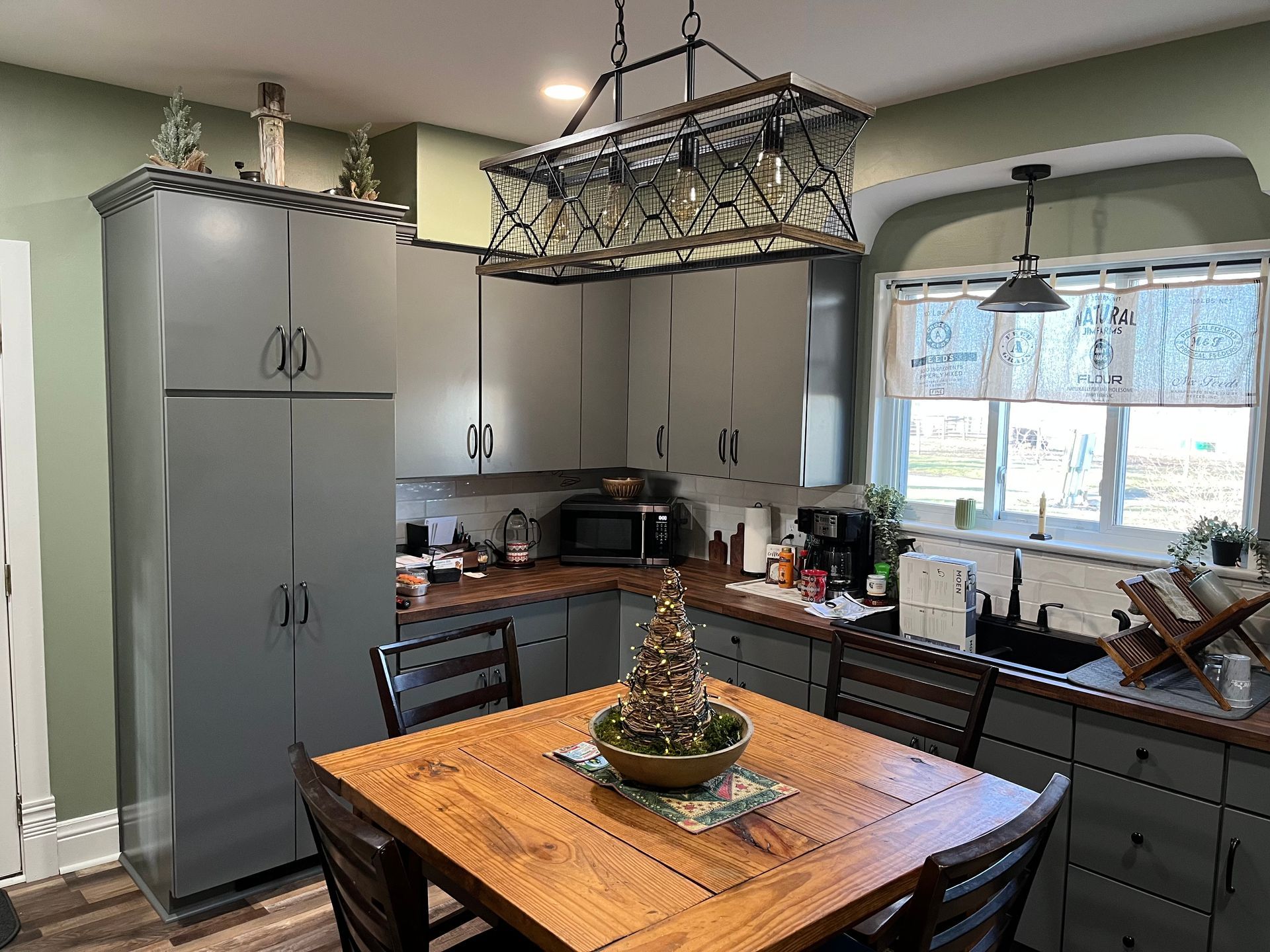 Bright kitchen with gray cabinets, wooden island table, and large window over the sink
