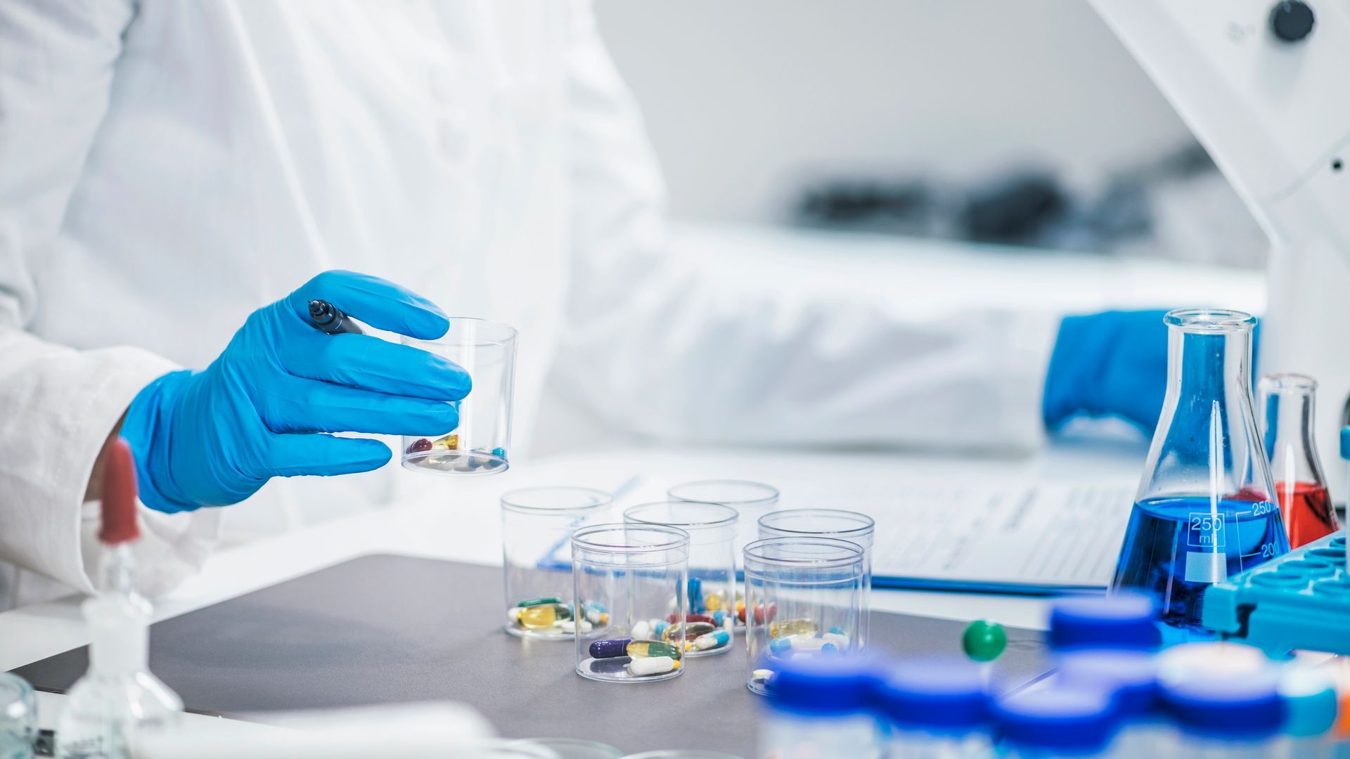 Scienziato in camice e guanti blu che tiene delle pillole in un becher