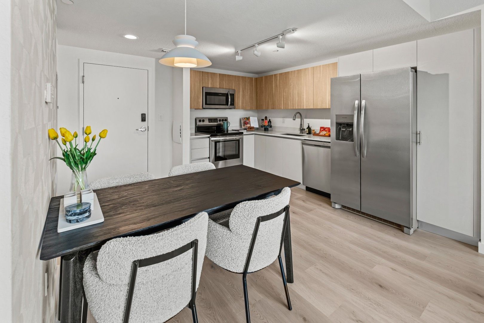 Modern kitchen with dining table, stainless steel appliances, light wood cabinets, and light flooring.