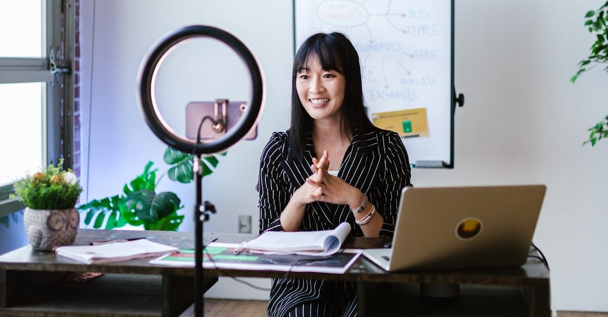 A woman is sitting at a desk with a laptop and a ring light.