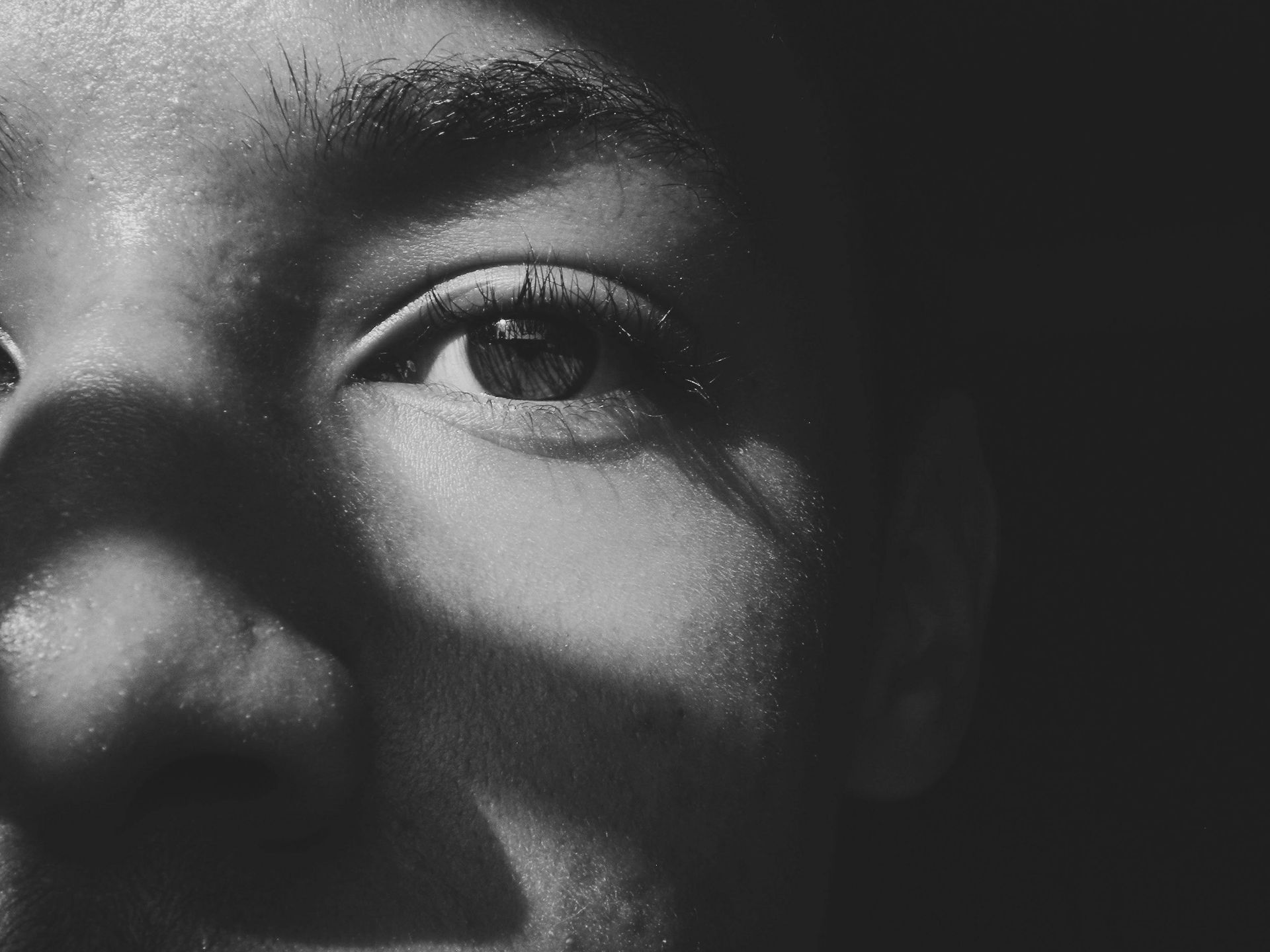 Close-up black-and-white portrait of a face with dramatic shadow across one eye