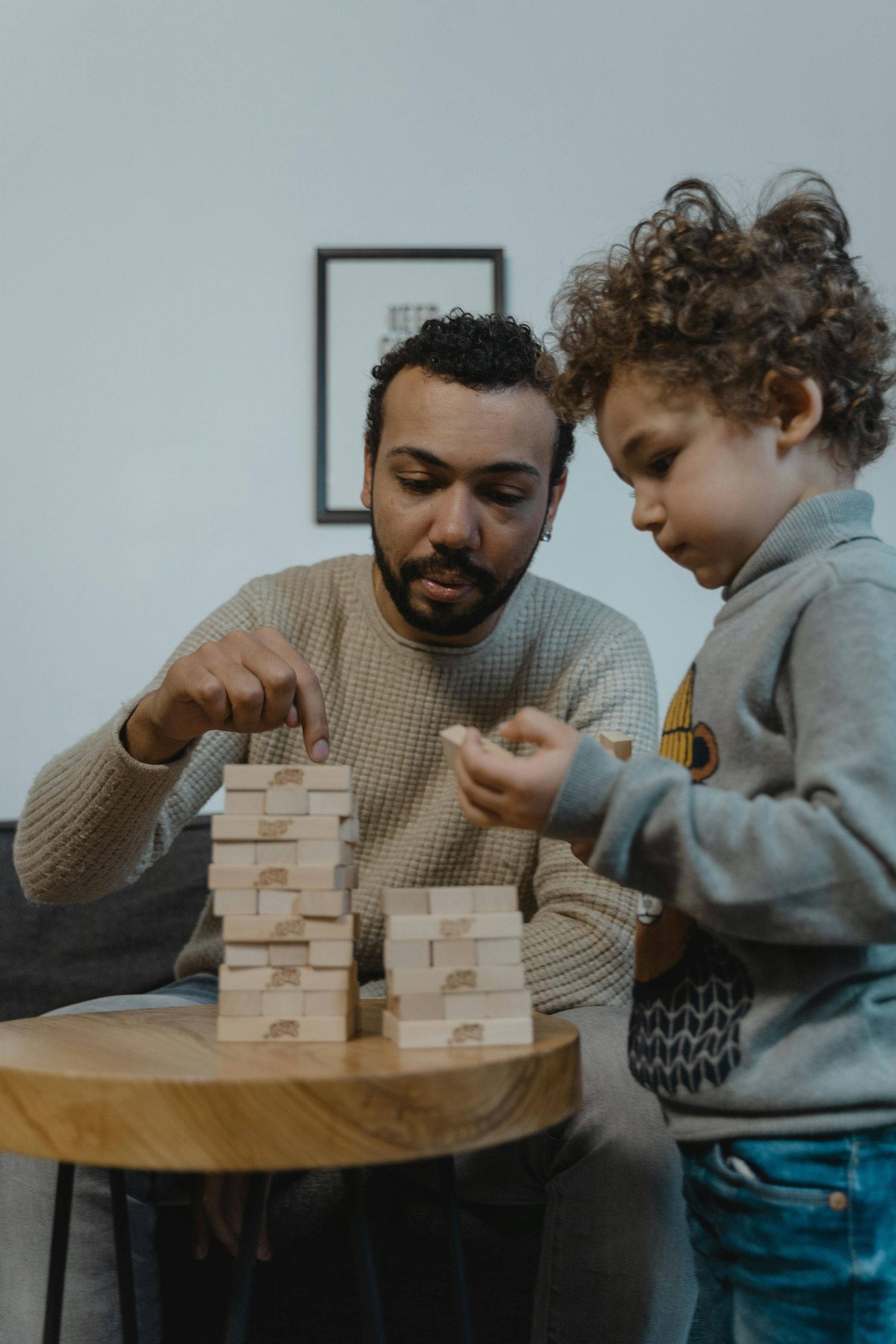 Two people building a wooden block tower at a table indoors