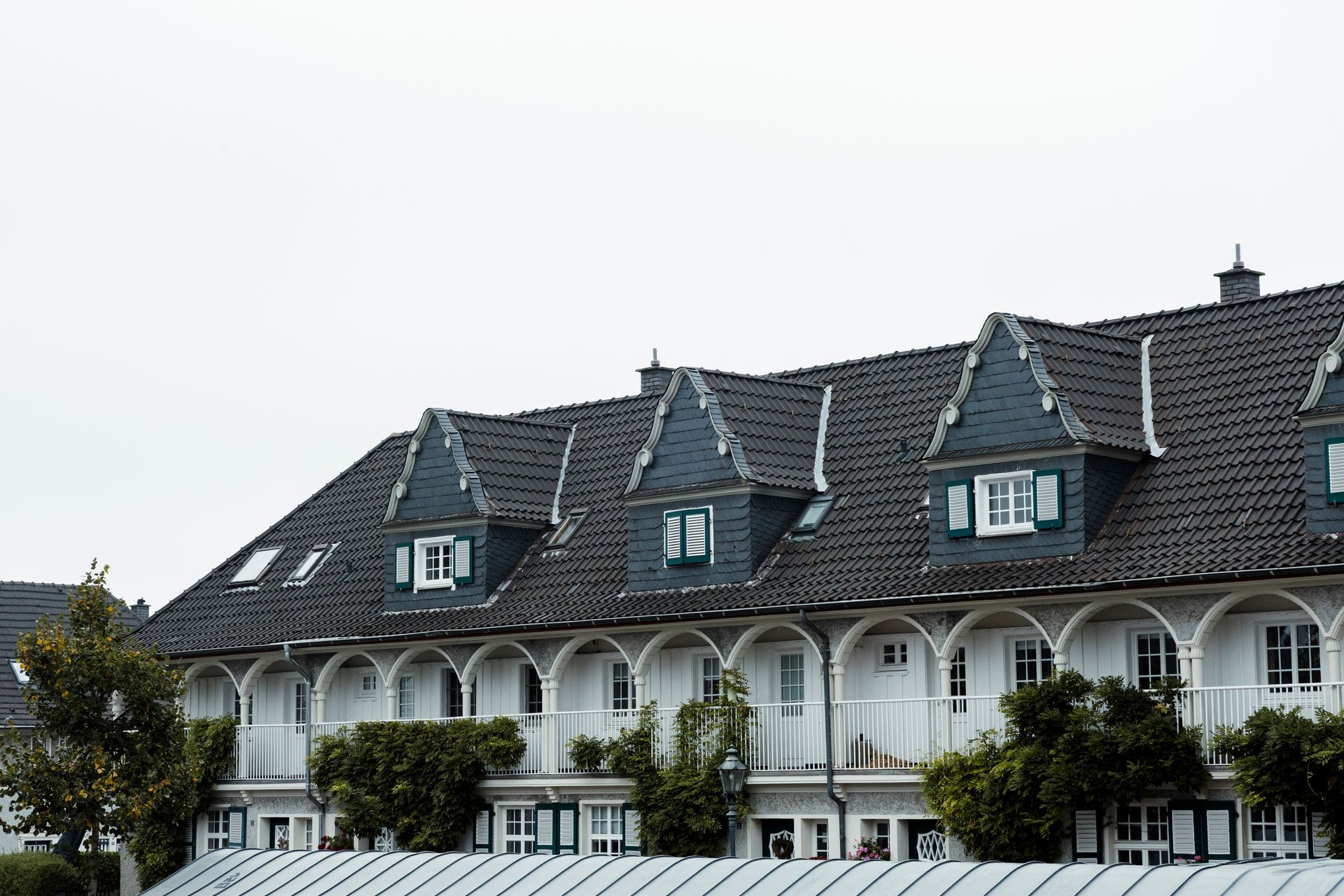 Eine Reihe weißer Stadthäuser mit dunkelgrauen Dächern, Bogenbalkonen und Dachgauben.