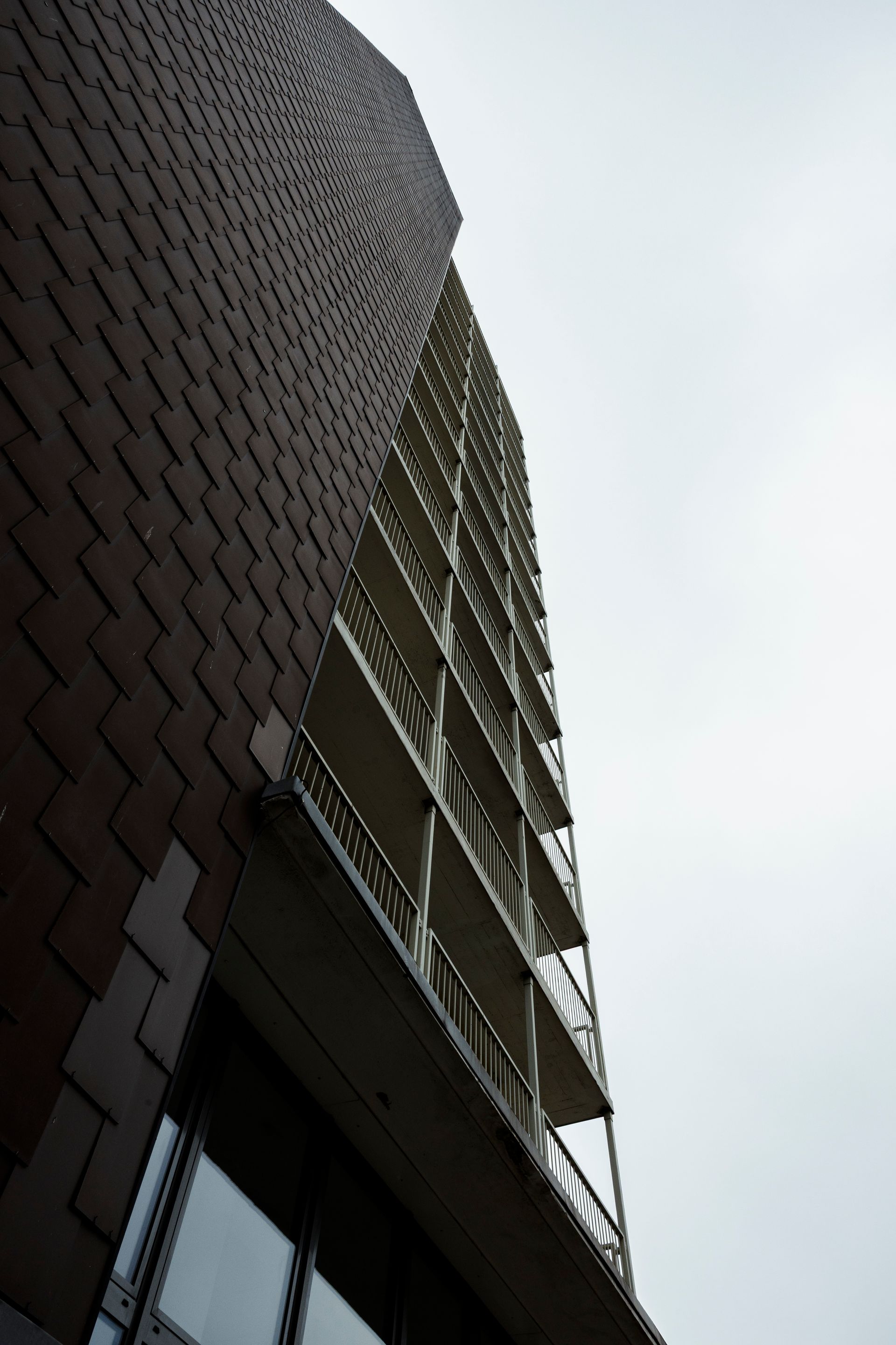 Froschperspektive auf ein hohes Backsteingebäude mit Balkonen vor bedecktem Himmel.