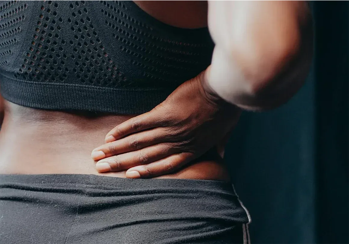 Person in dark athletic wear, touching lower back in pain.