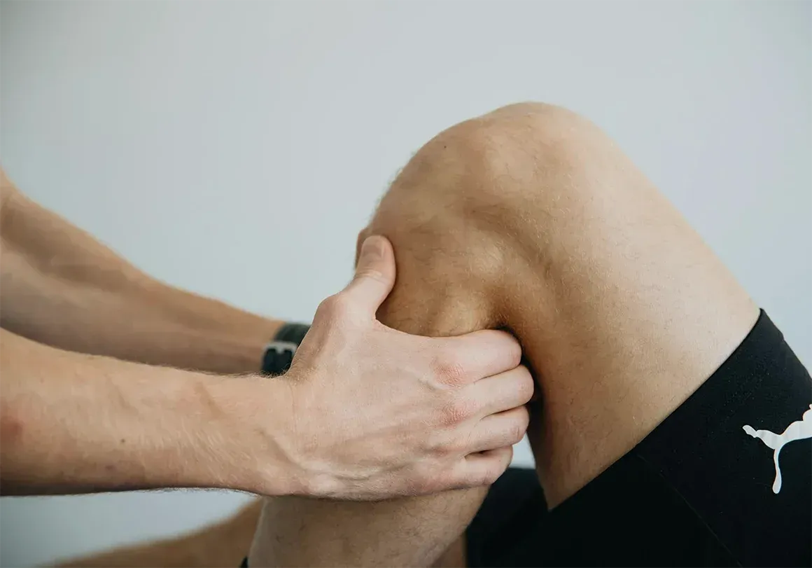 Hands examining a person's knee. The knee is bent, and the hands are placed around it.
