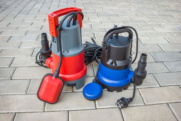 Two submersible water pumps with float switches on a brick surface. Two submersible water pumps with float switches on a brick surface.