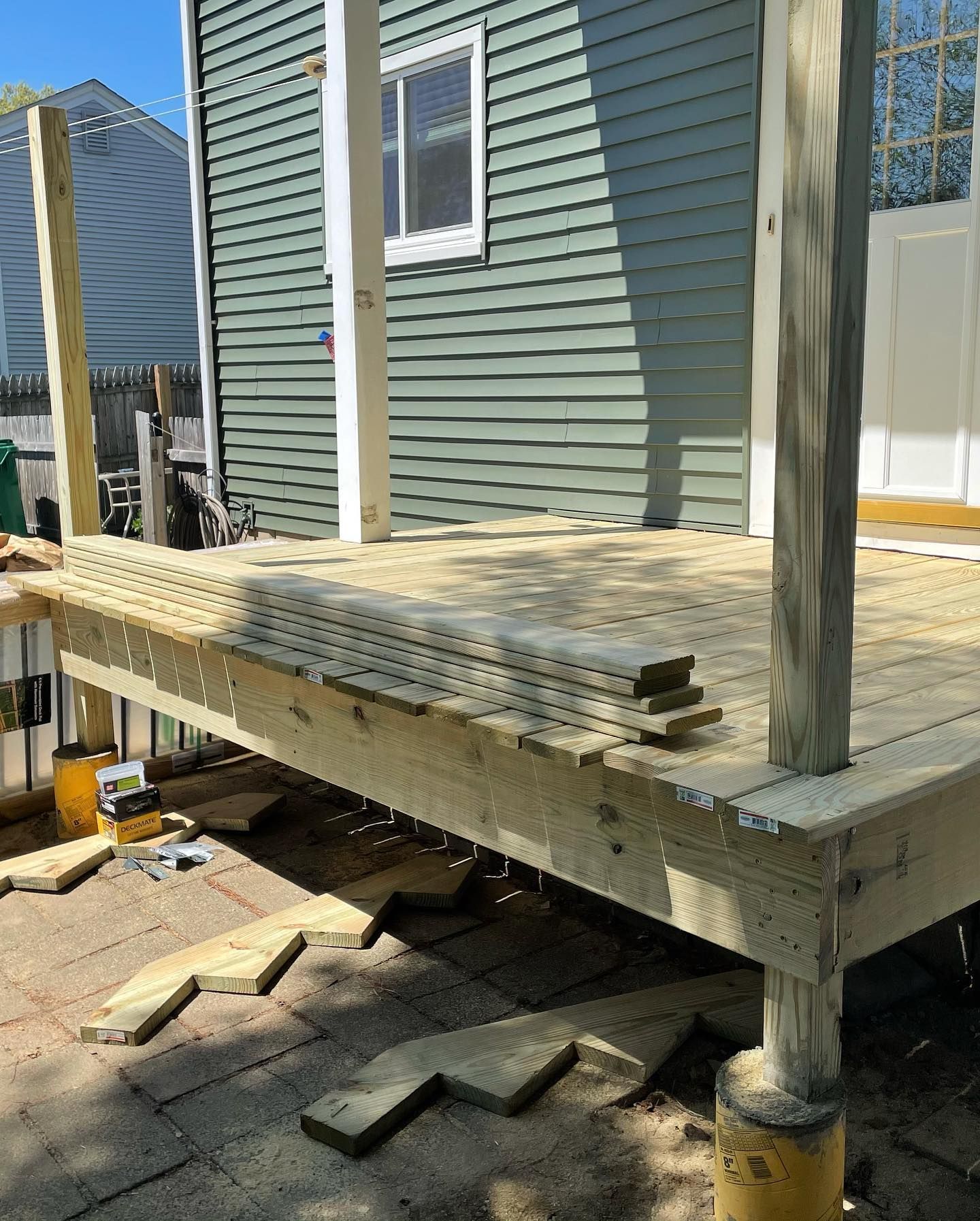A partially built wooden deck with several support posts against a green house.