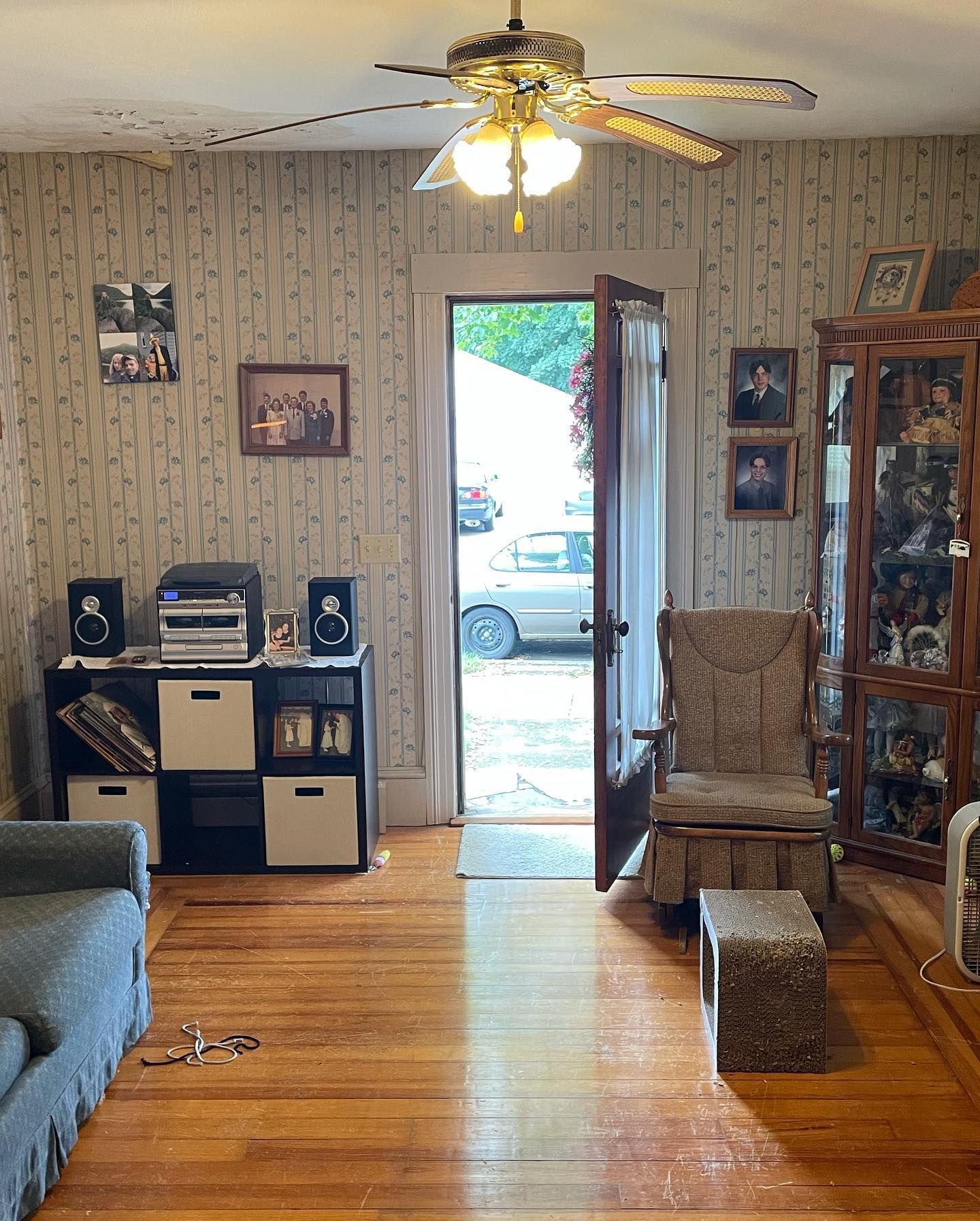 Living room with wood floor, stereo, open door. Patterned wallpaper, antique furniture.