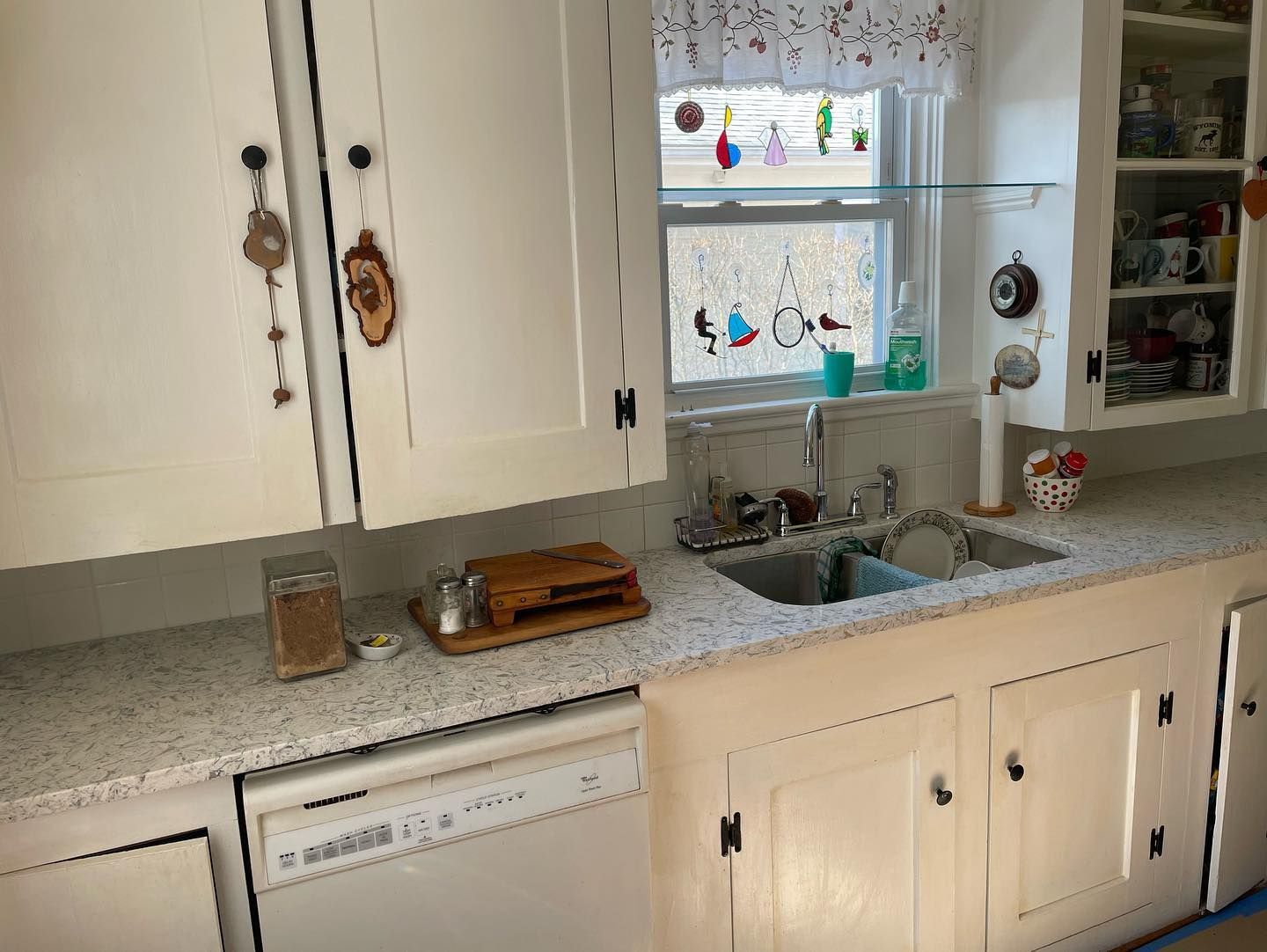 White kitchen cabinets and countertops with a window, sink, and dishwasher.