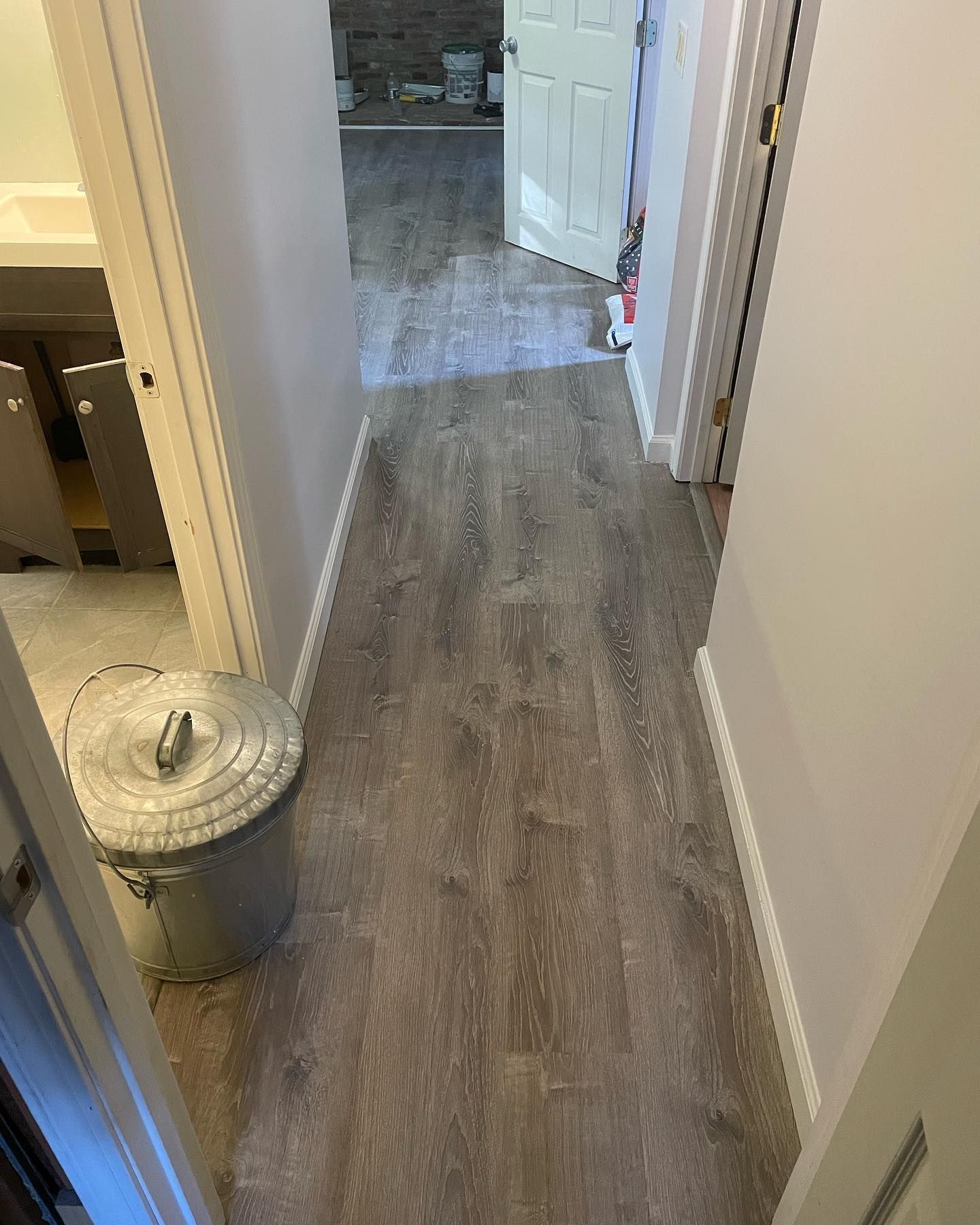 Hallway with wood-look flooring and white trim. Gray trash can near door. Pink walls and open doorways.